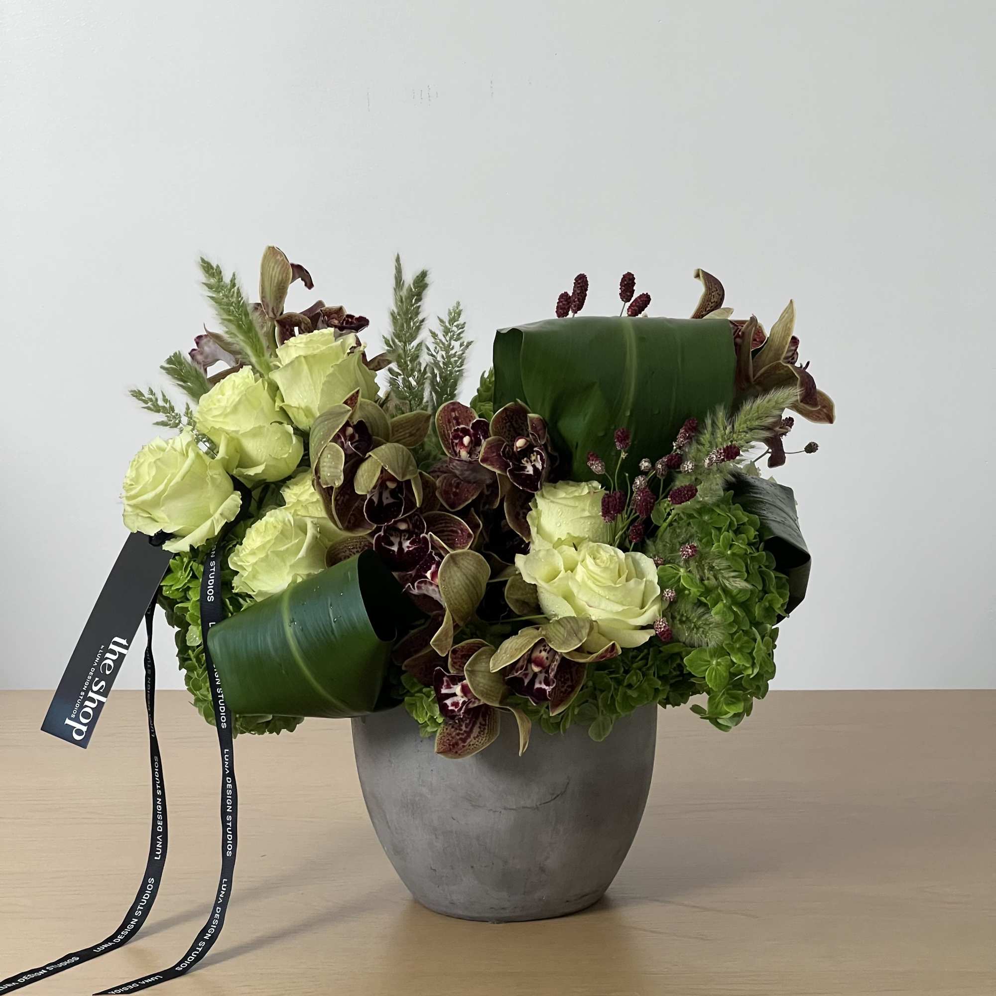 Green and burgundy floral arrangement in a gray vase