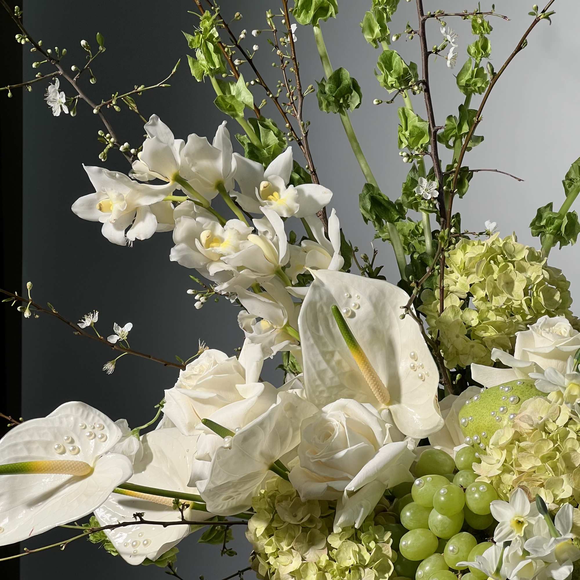 White orchids, roses, and calla lilies arranged with green hydrangeas and grapes