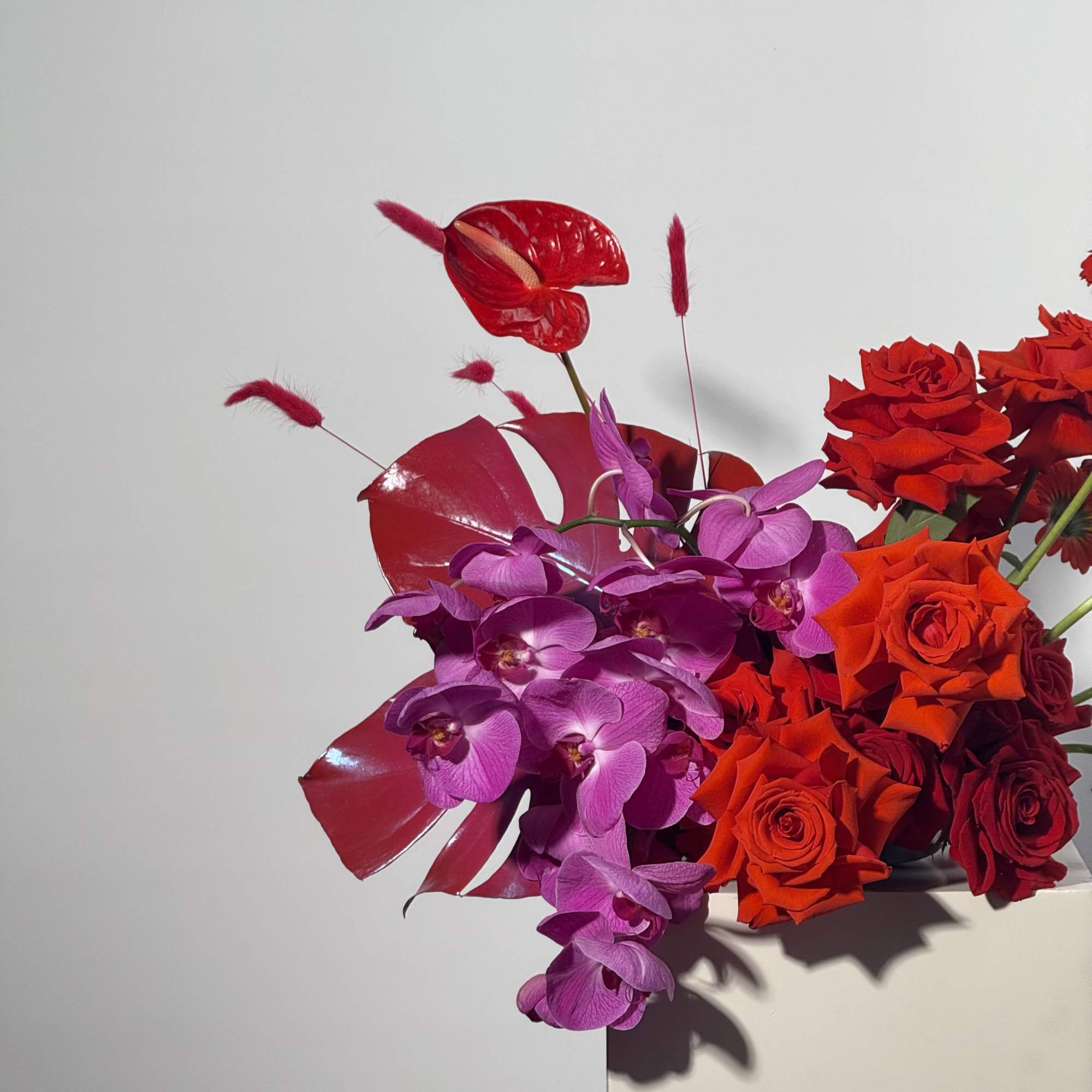 Red roses and purple orchids in a white container