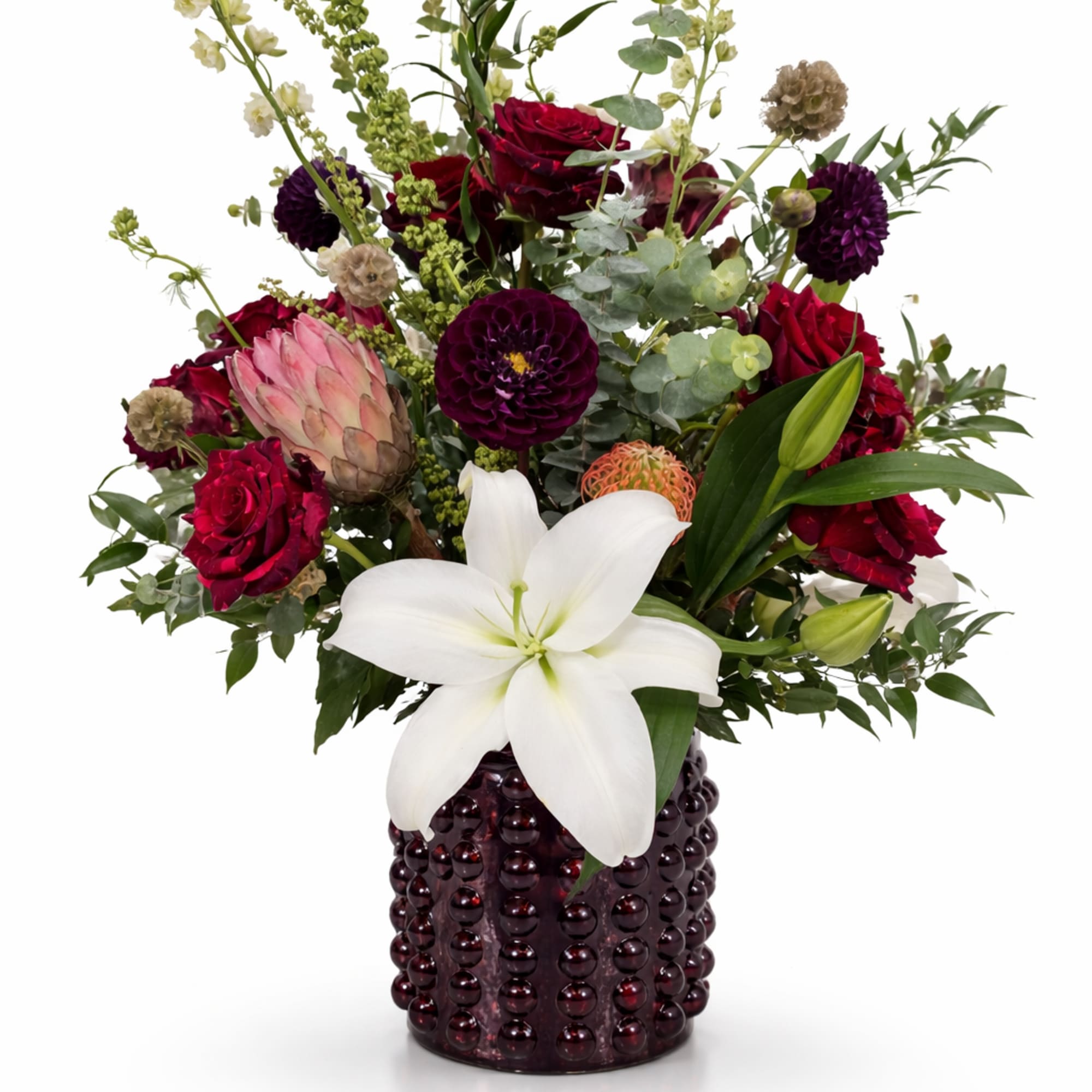 Bouquet of red roses, white lily, and purple blooms in a dark beaded vase