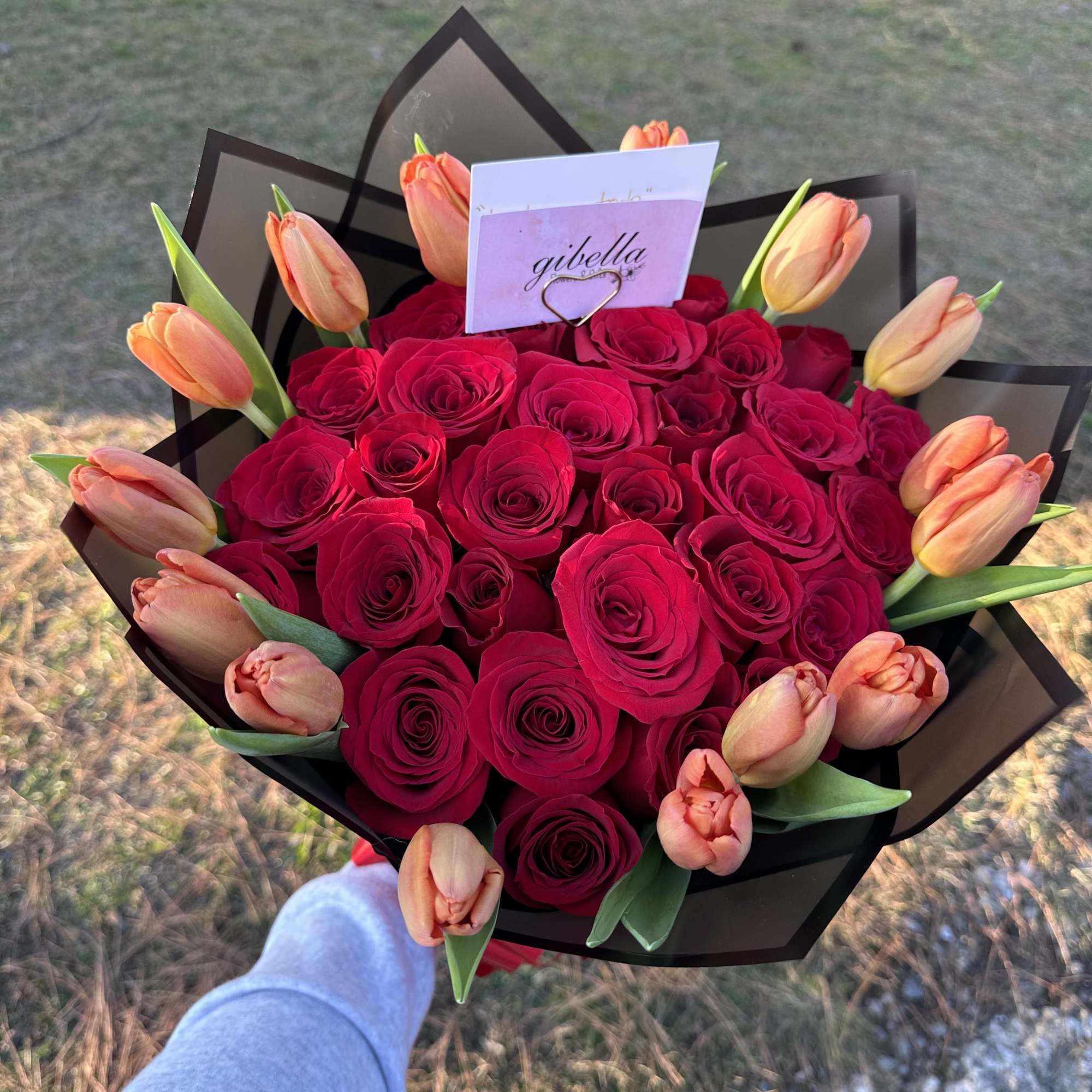 Bouquet of red roses with peach tulips wrapped in black paper