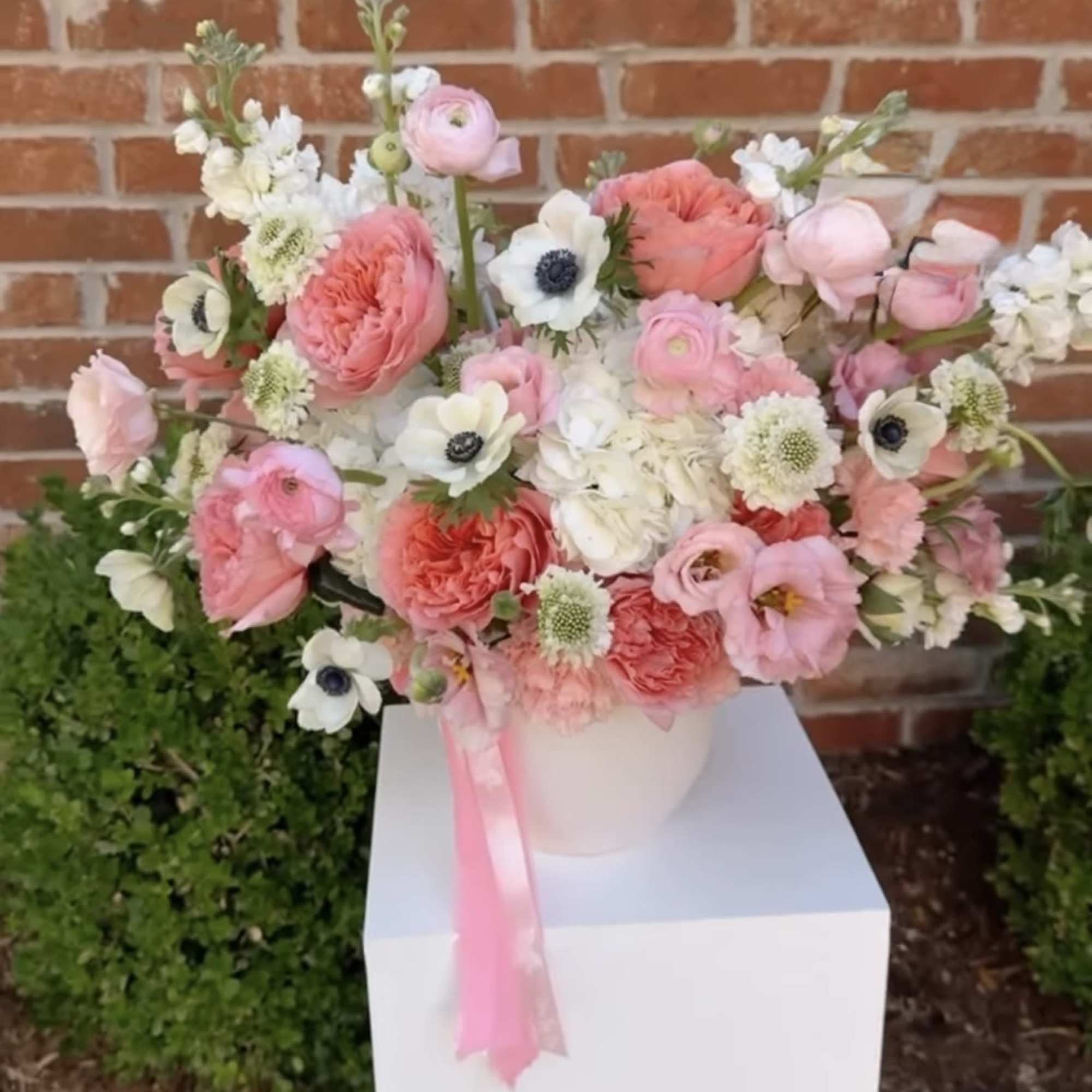 Pink and white mixed flower arrangement in a white vase with a pink ribbon