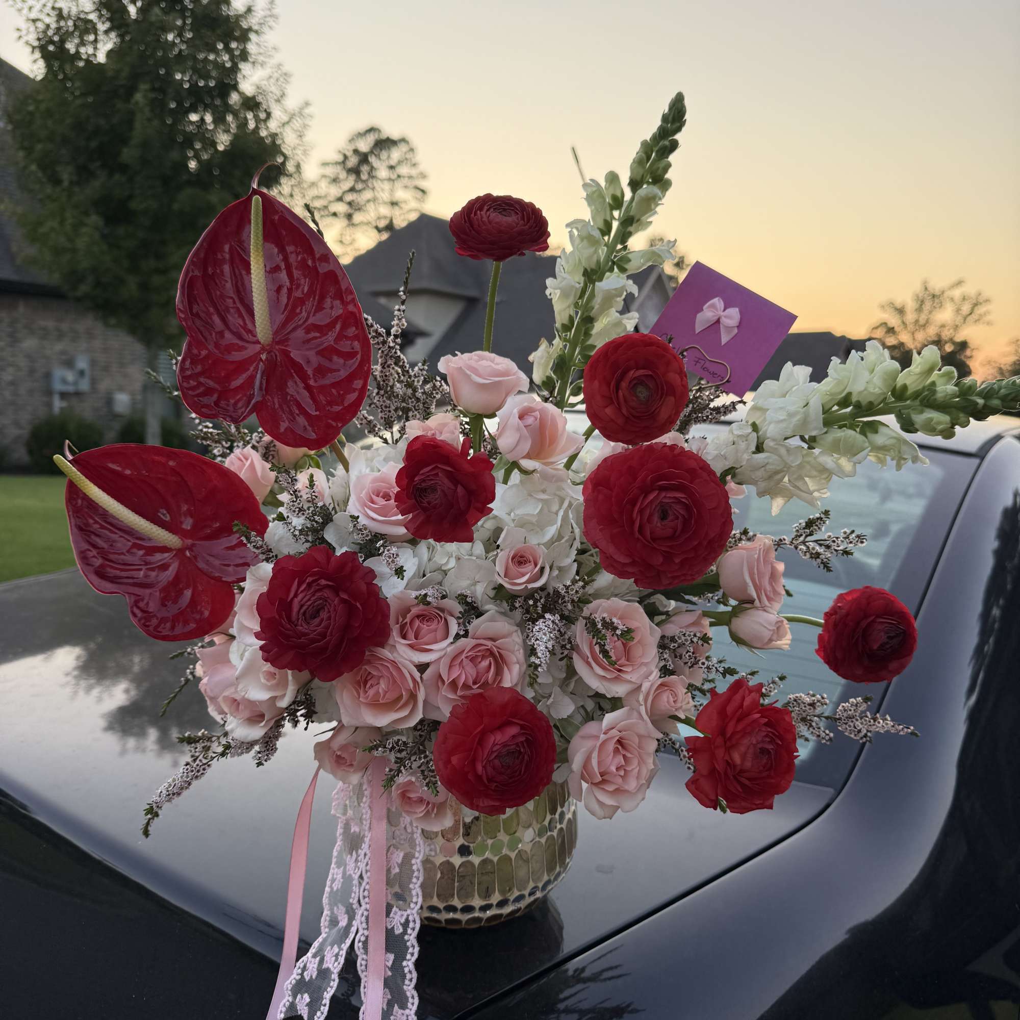 Bouquet of red anthuriums, pink roses, and white flowers in a patterned vase