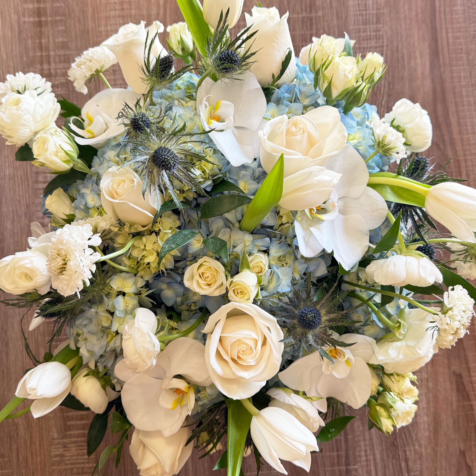 White roses and orchids arranged with pale blue hydrangeas in a bouquet.
