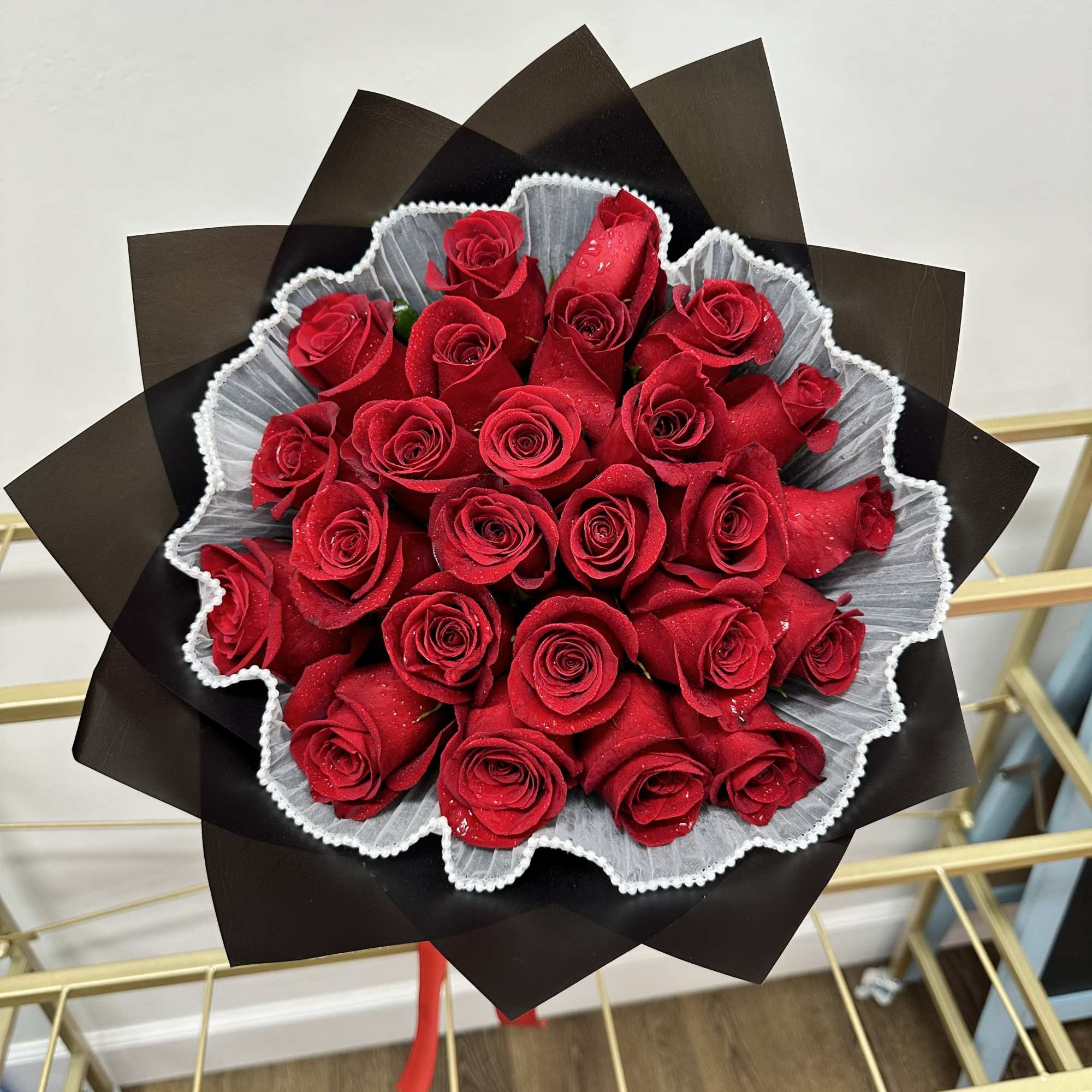 This striking arrangement features vibrant red roses, beautifully wrapped in sophisticated black