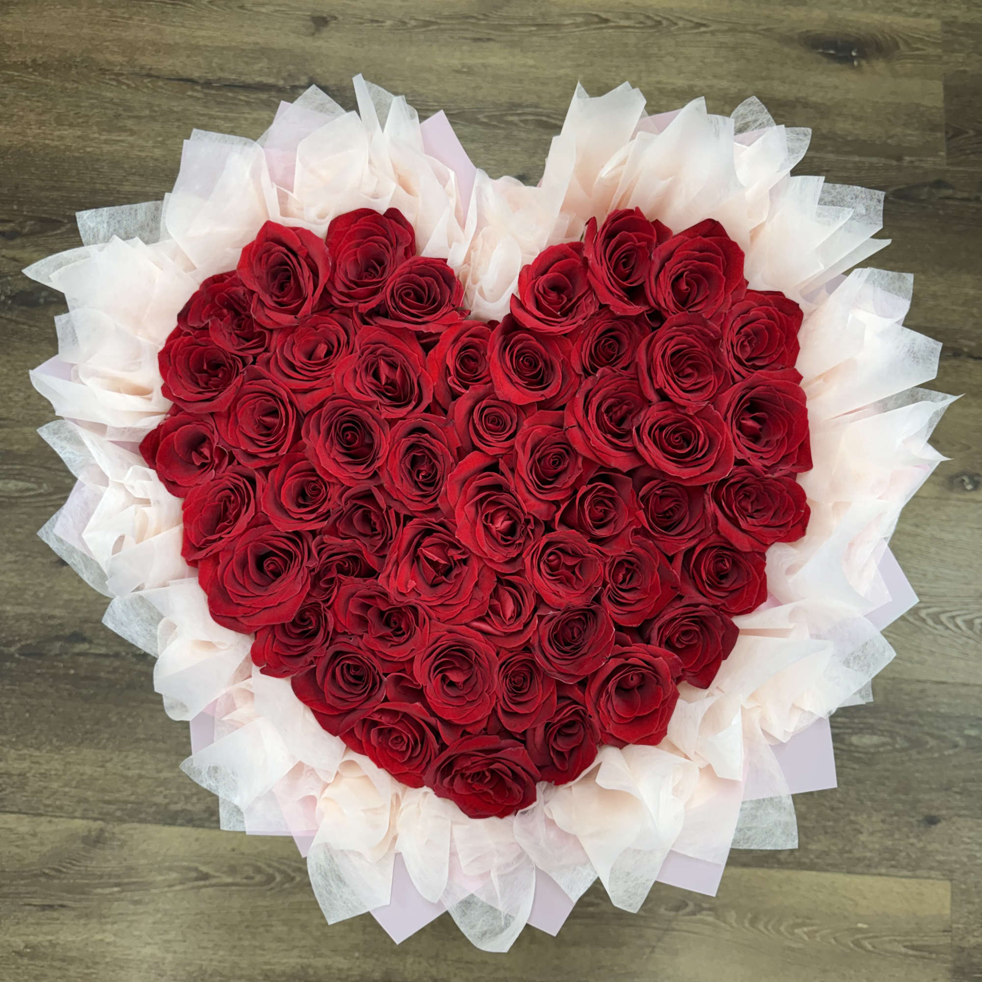 Heart-shaped bouquet of red roses wrapped in pale tissue paper