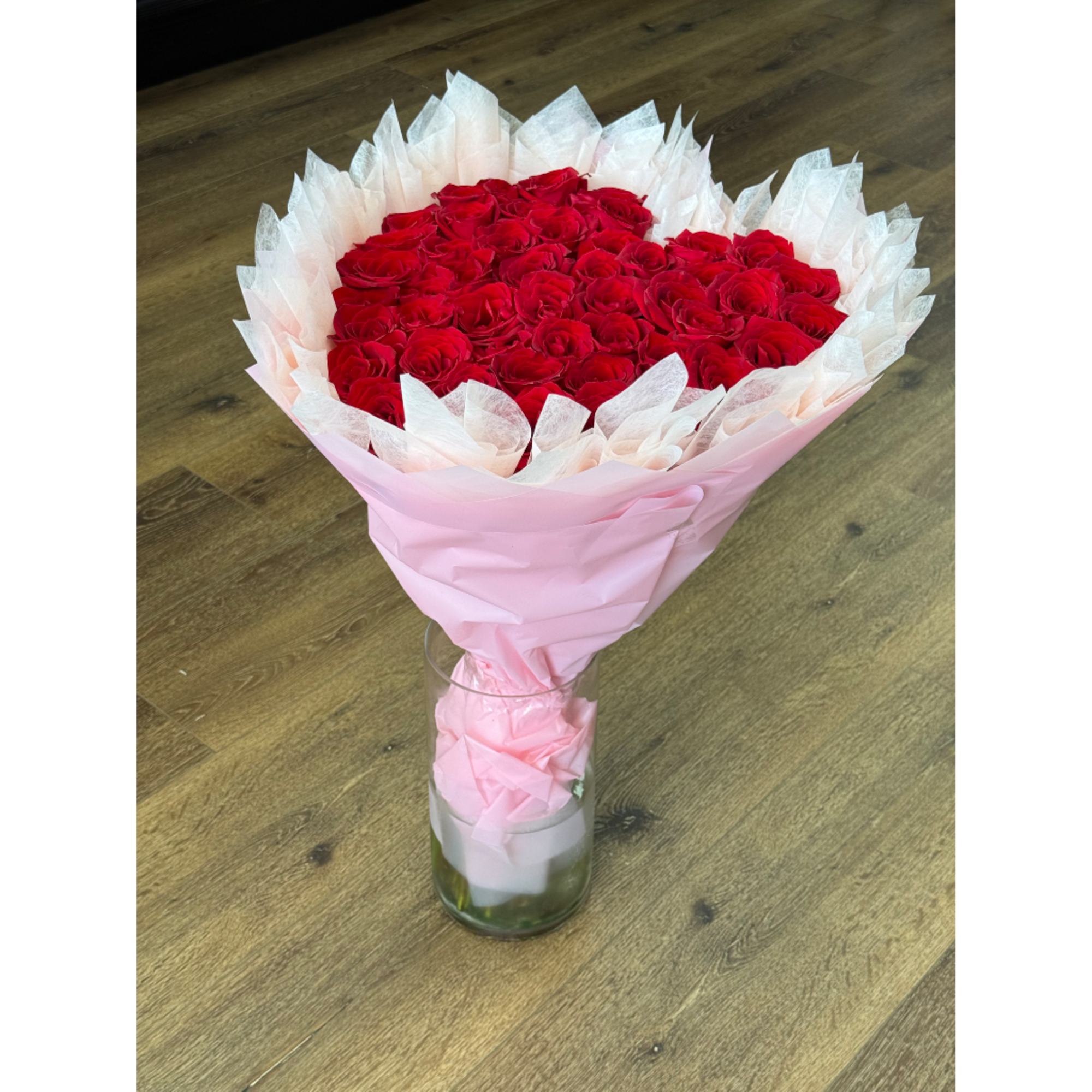 Bouquet of red roses wrapped in pink and white paper in a glass vase