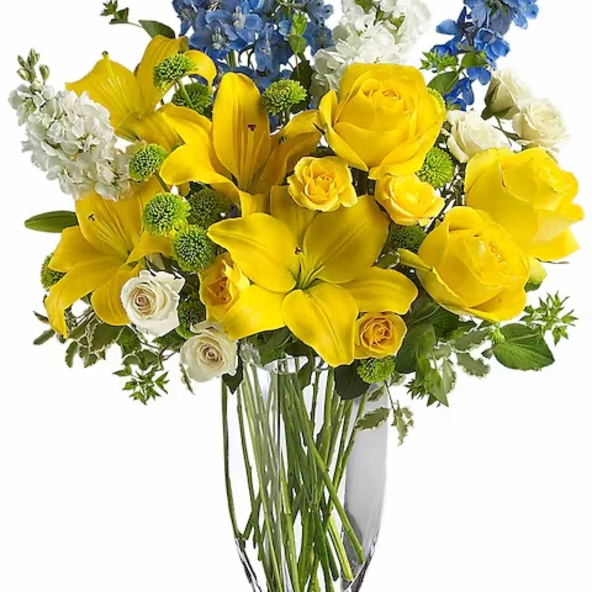 Yellow roses and lilies with blue and white flowers in a clear vase