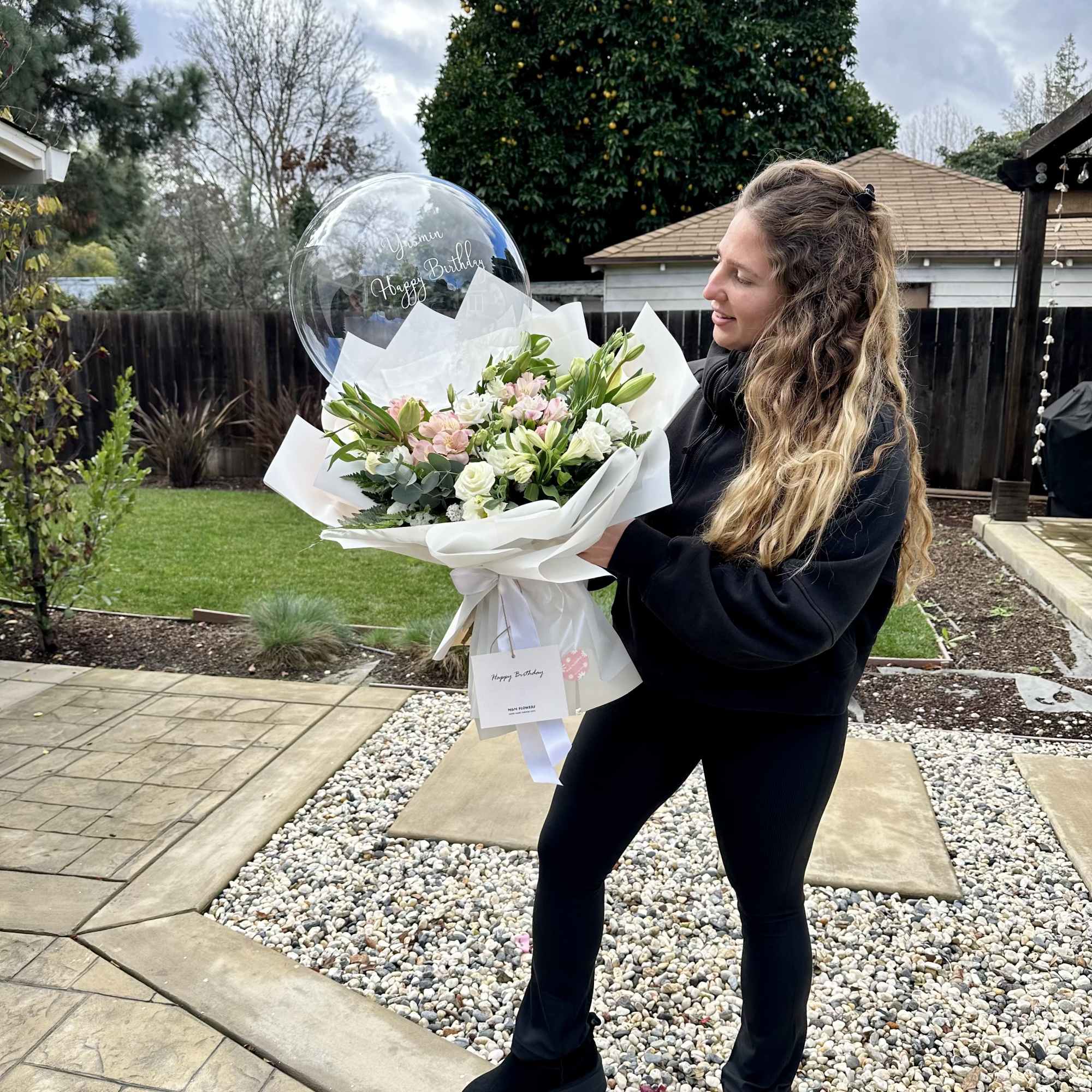 Woman holding a wrapped bouquet with a clear birthday balloon