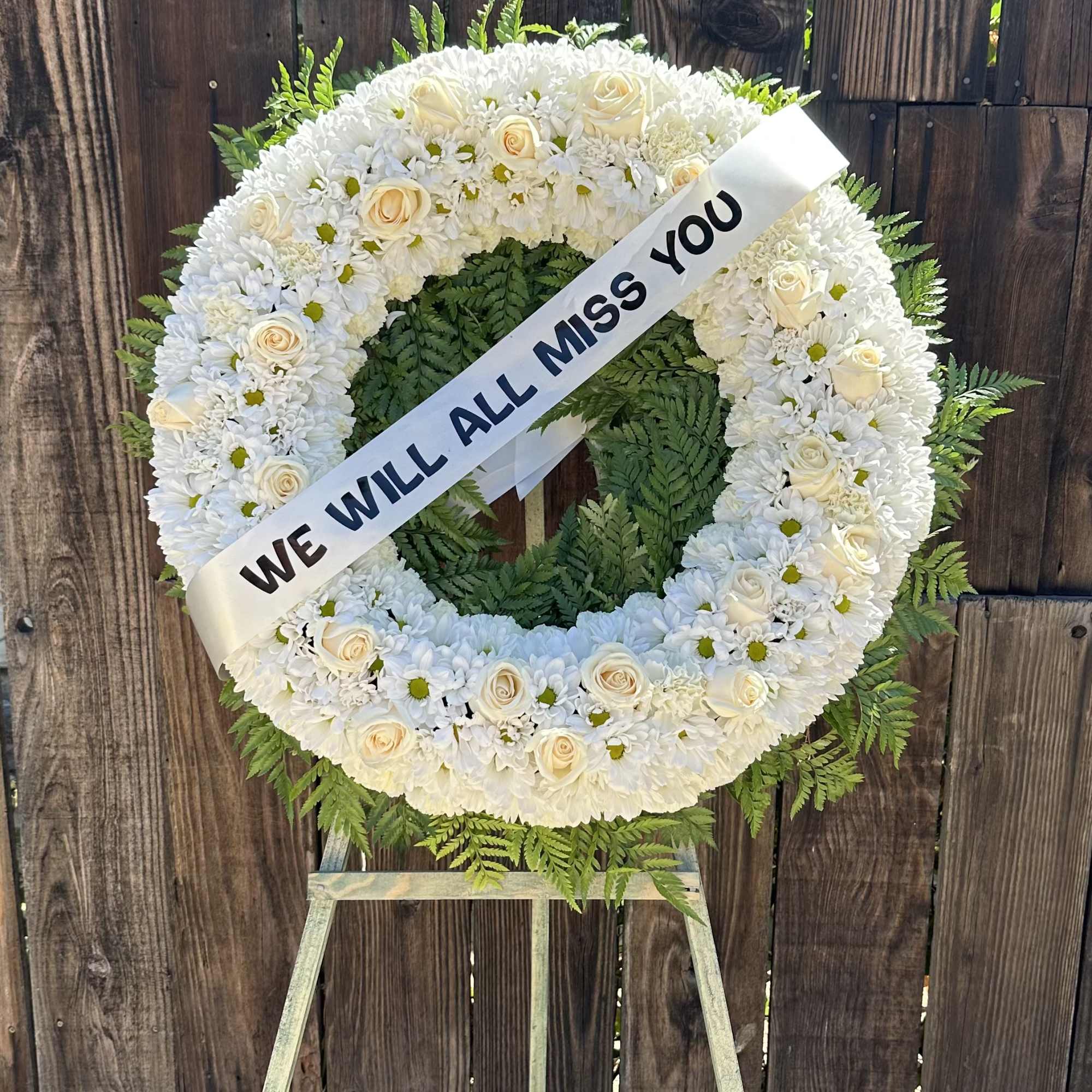 White funeral wreath on an easel with a memorial ribbon