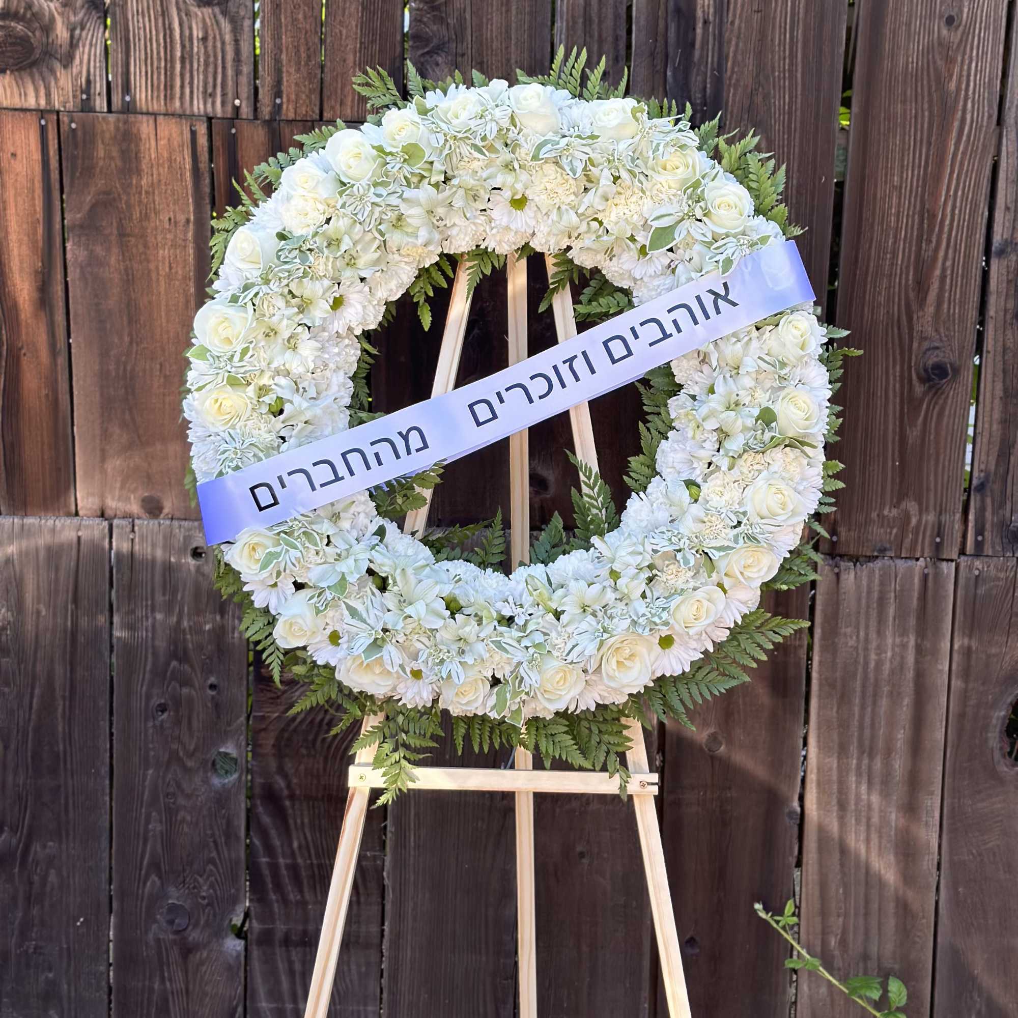 White floral wreath on a wooden easel with a ribbon across it