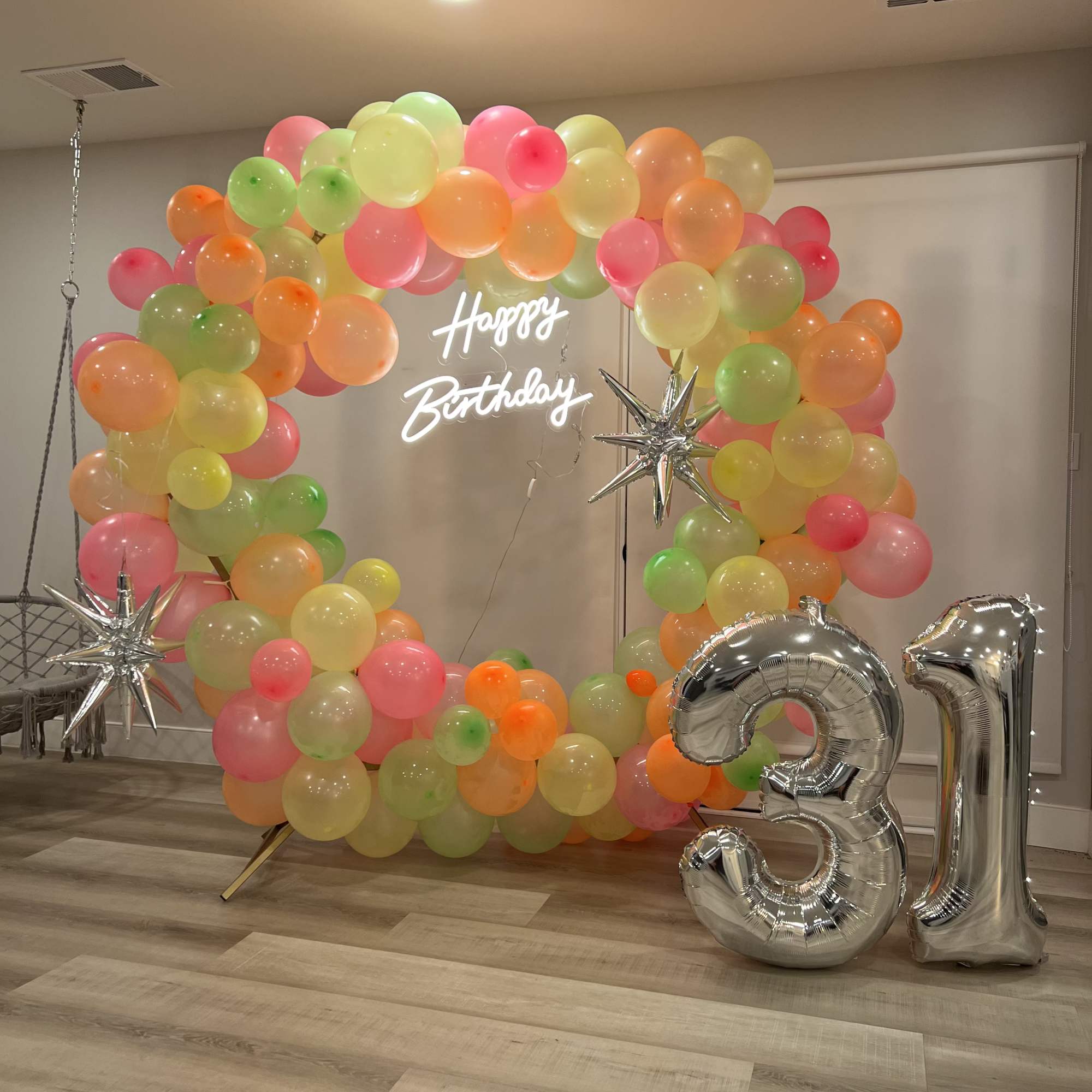 Colorful balloon arch with a neon Happy Birthday sign and silver 31 balloons