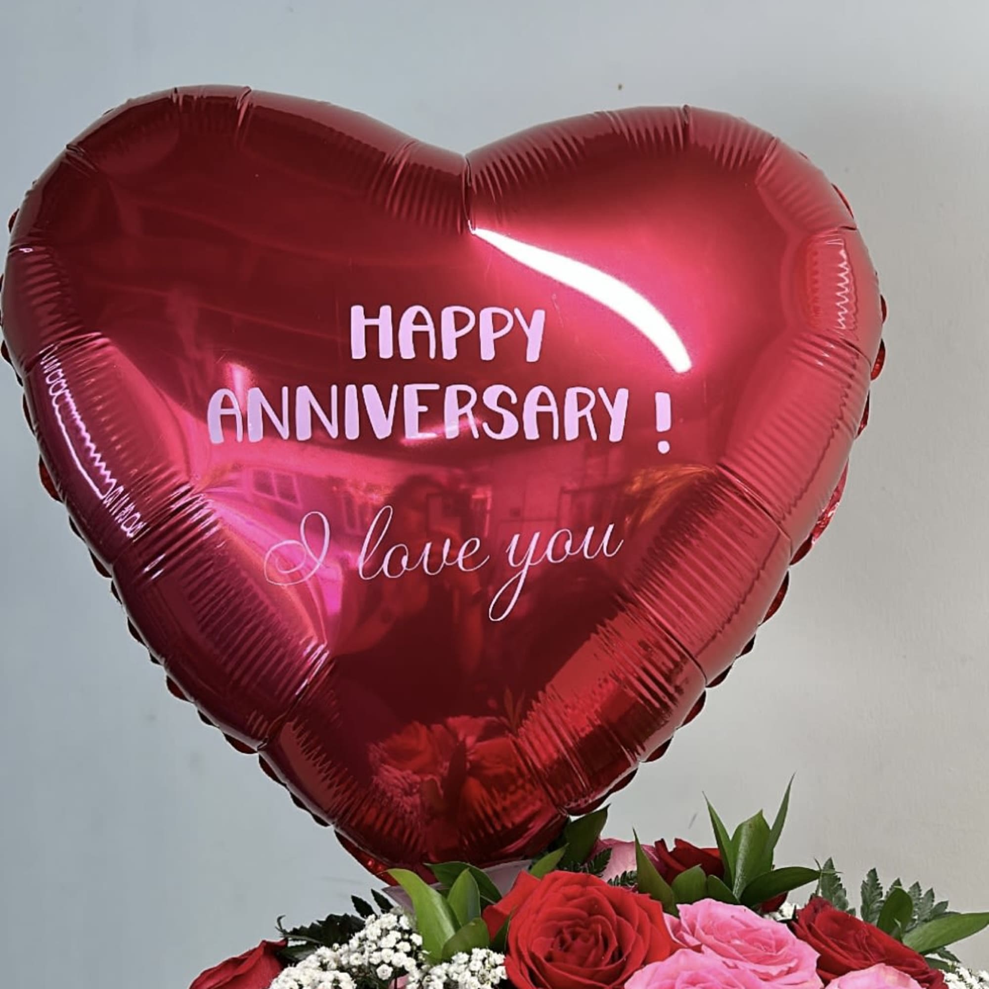 Heart-shaped red anniversary balloon above a bouquet of red and pink roses
