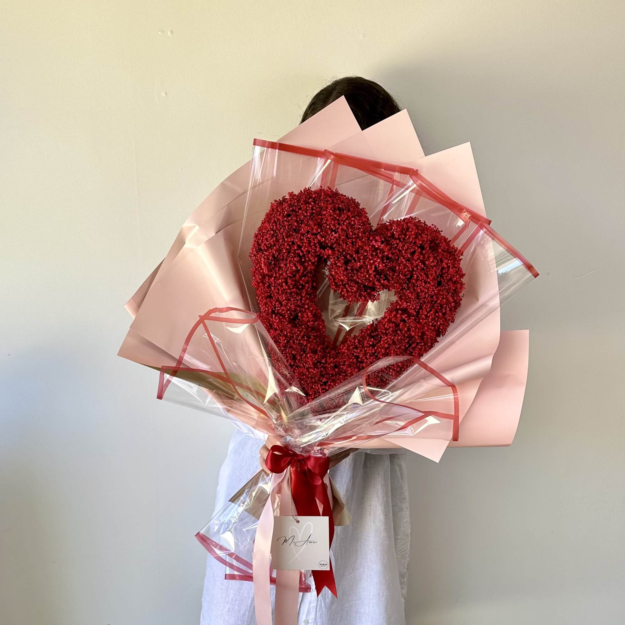 Heart-shaped red flower bouquet wrapped in pink paper and clear plastic