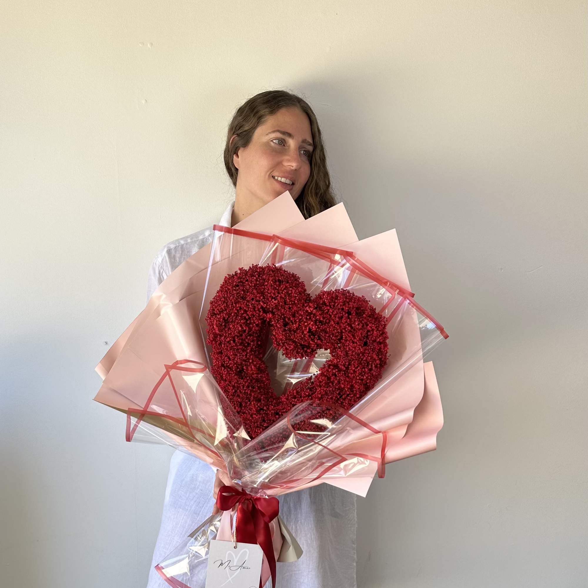 Woman holding a heart-shaped red flower bouquet wrapped in pink paper