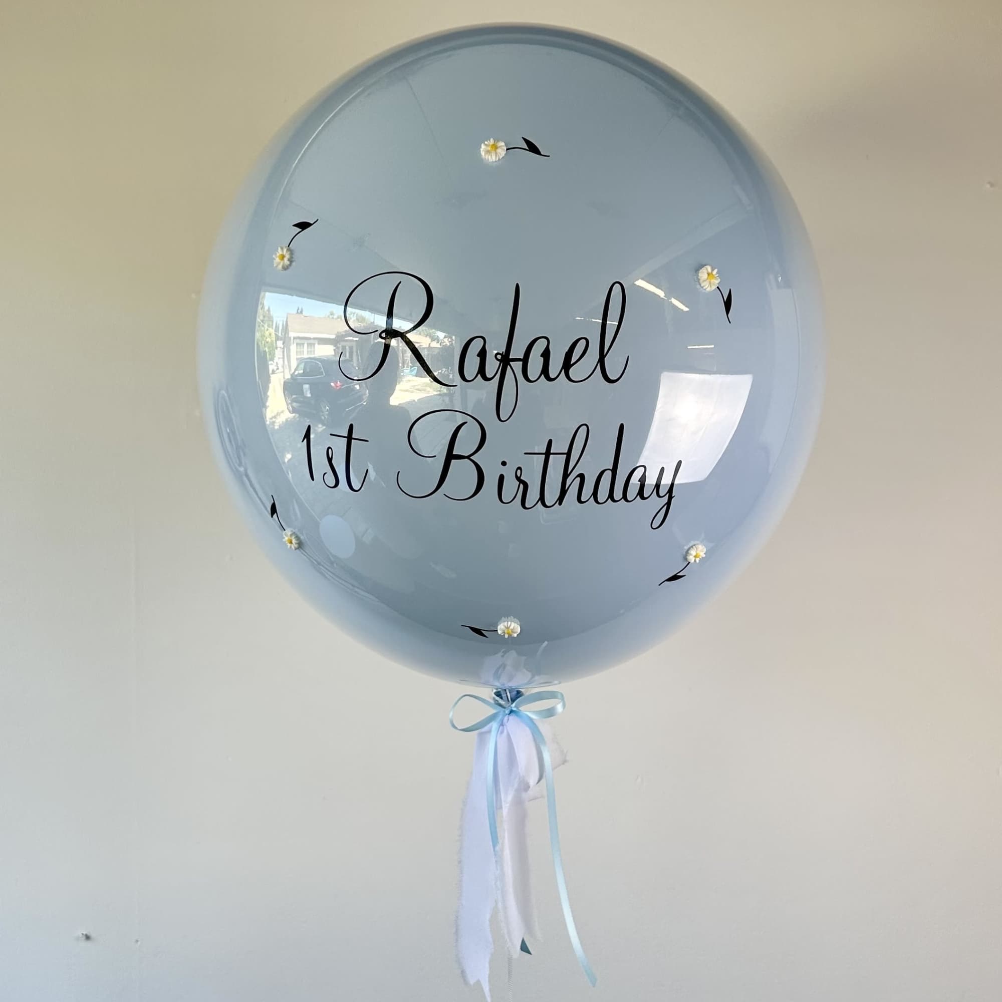 Light blue balloon with "Rafael 1st Birthday" text and ribbon tails
