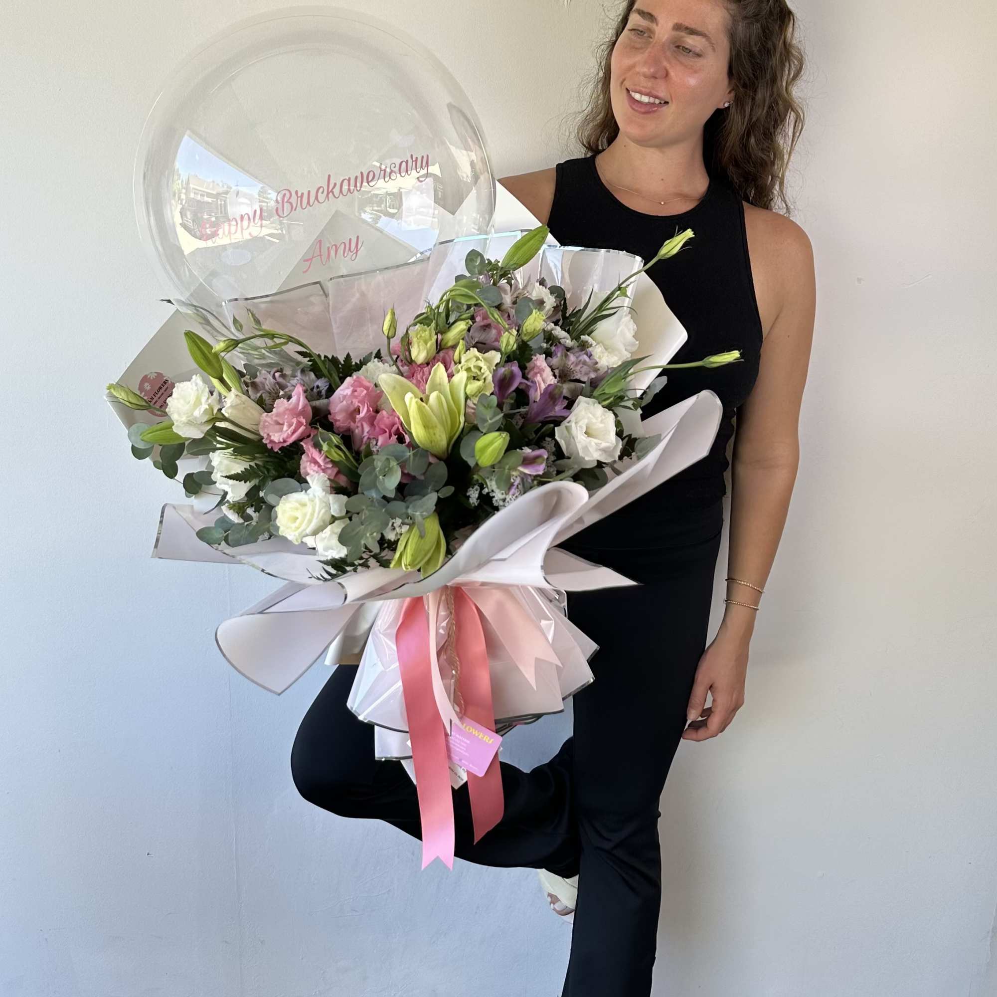 Woman holding a large bouquet with a clear balloon and pink ribbon