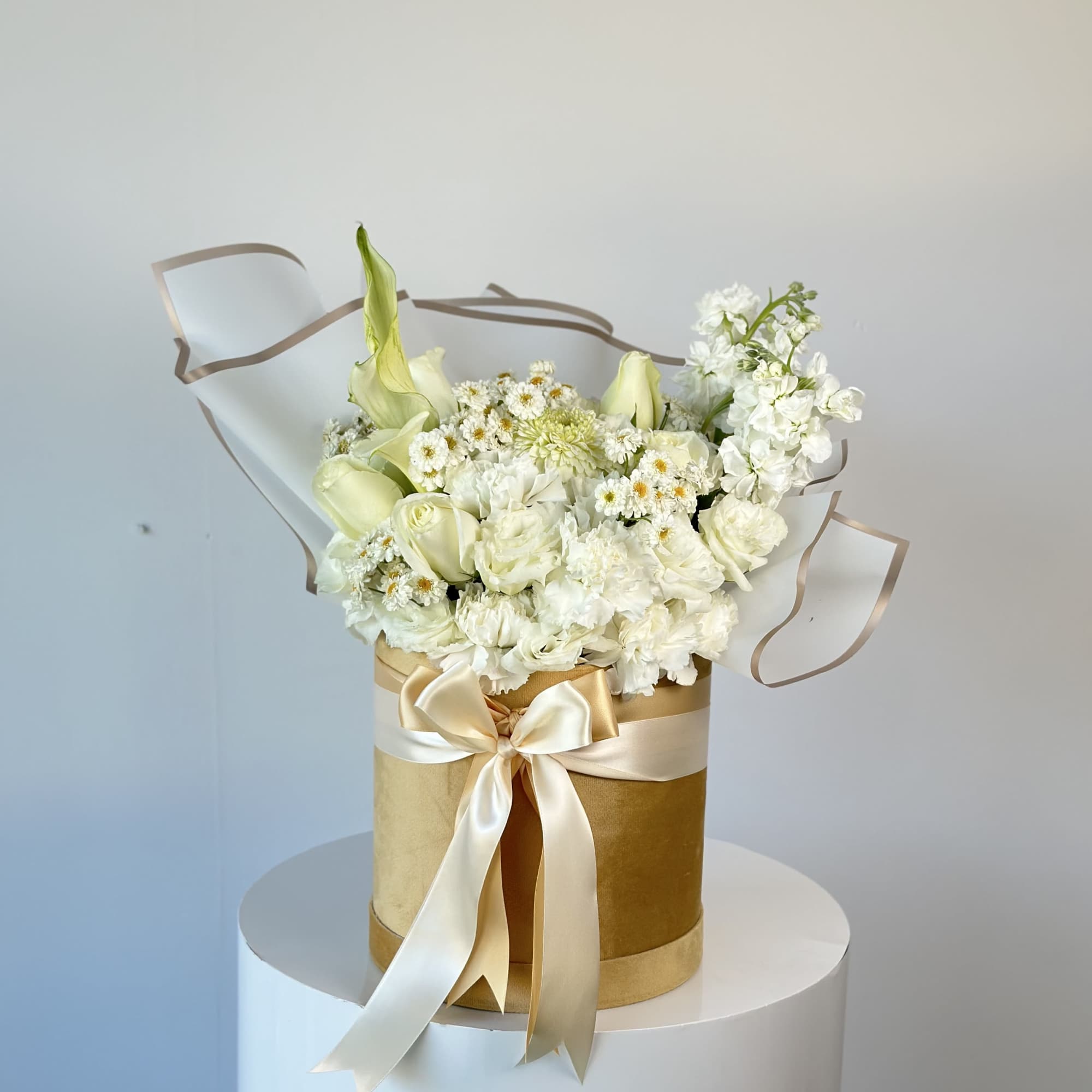 White floral bouquet in a gold hatbox with a satin ribbon