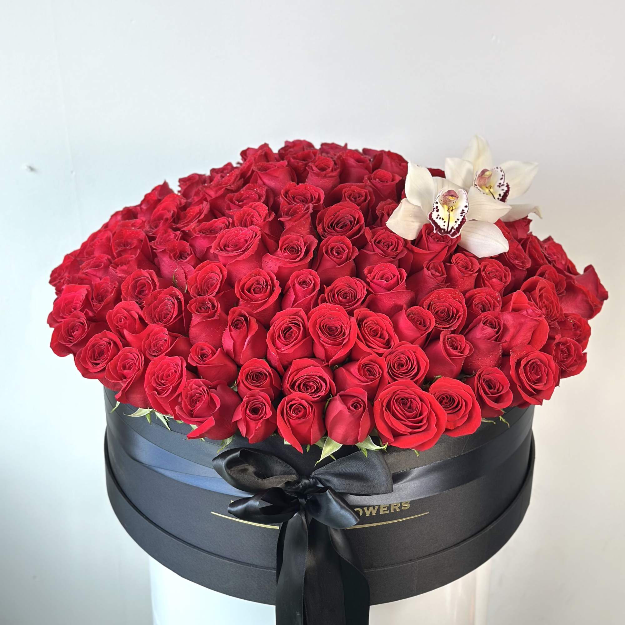 Large box of red roses with white orchids and a black ribbon