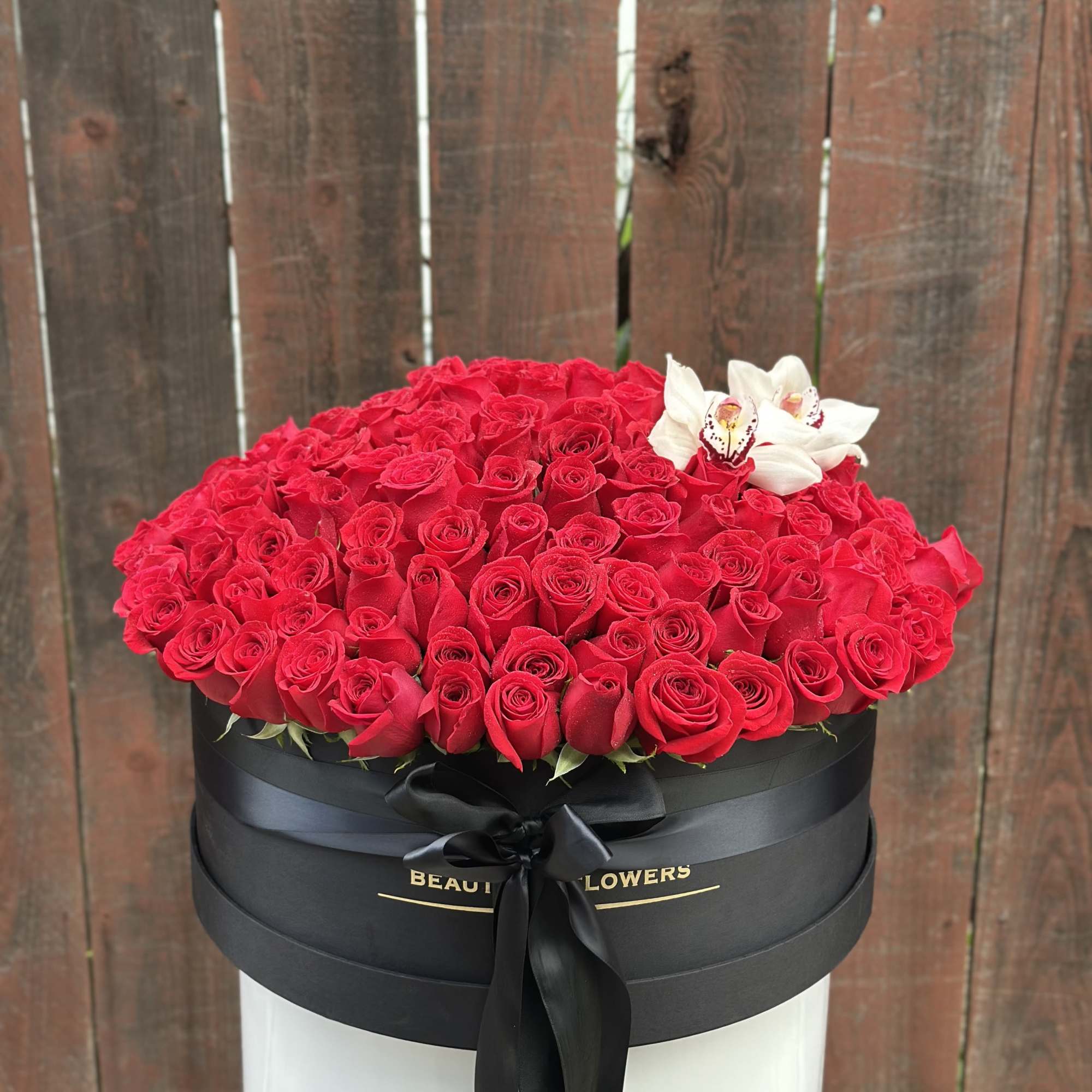 Large round box of red roses with white orchids on top