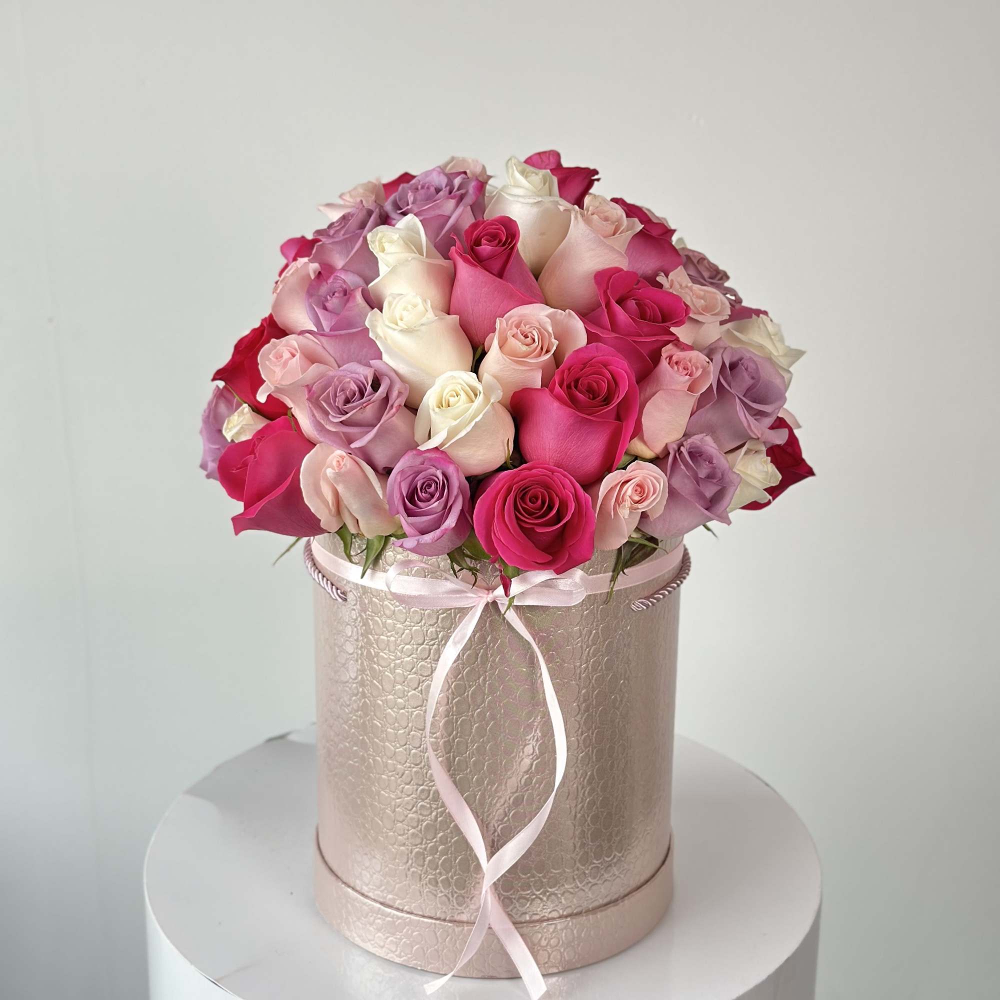 Pink and lavender roses arranged in a round hatbox with a ribbon