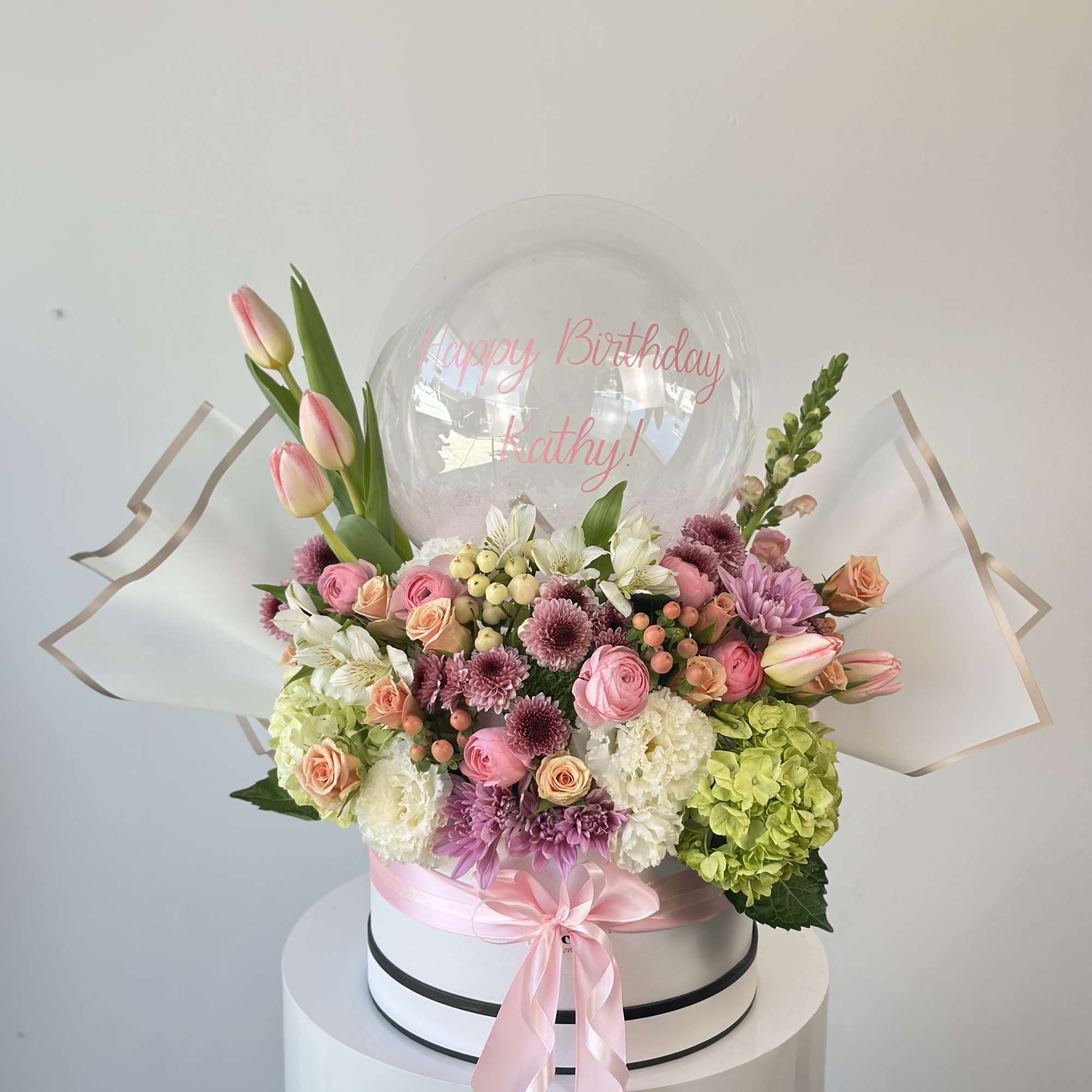 Pink and white floral arrangement with a birthday balloon and ribbon