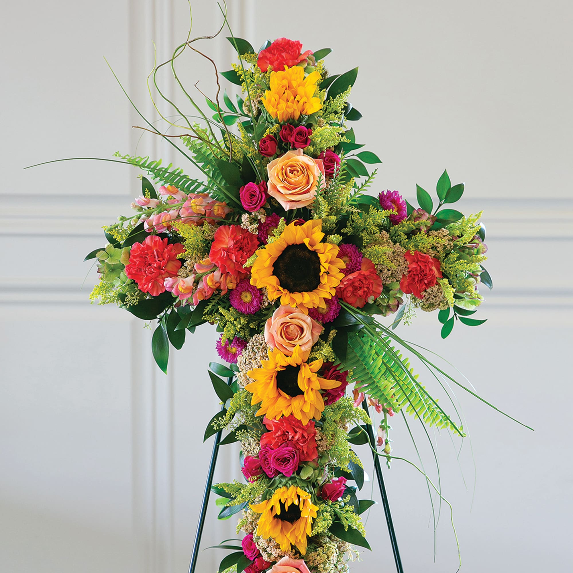 Tall floral cross with sunflowers, roses, and carnations on an easel