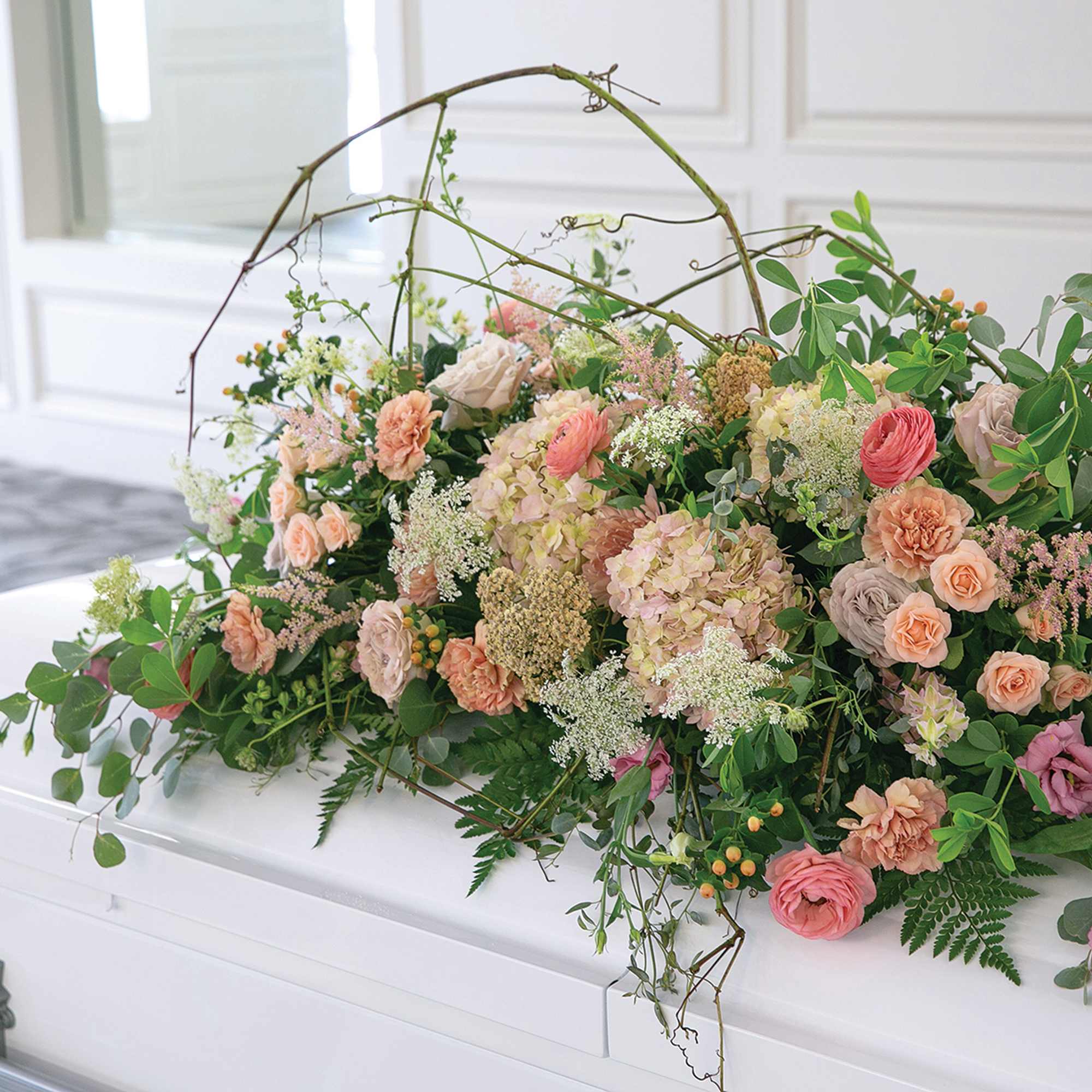 Pastel floral casket spray with roses and hydrangeas on a white casket