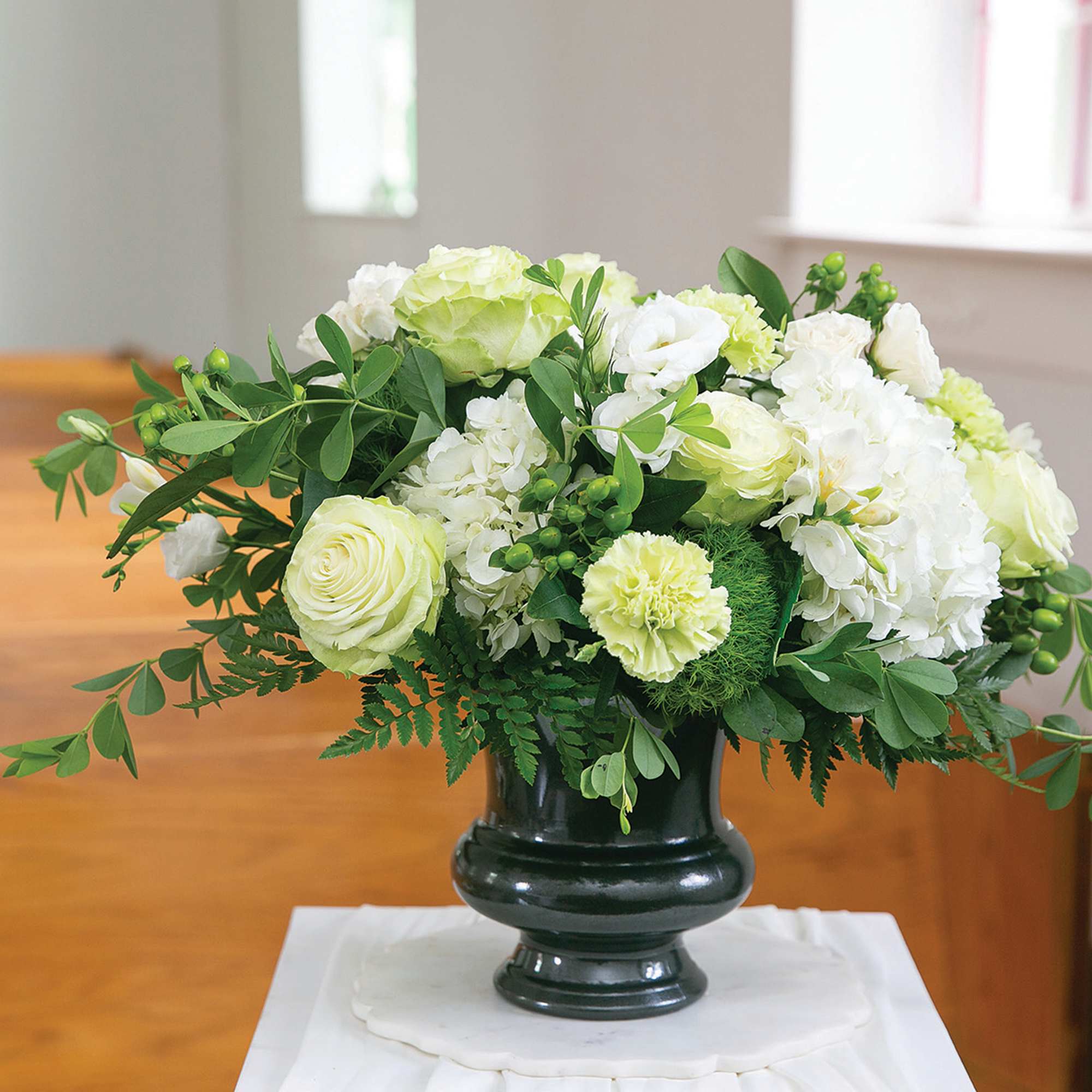 White and pale green floral arrangement in a dark vase