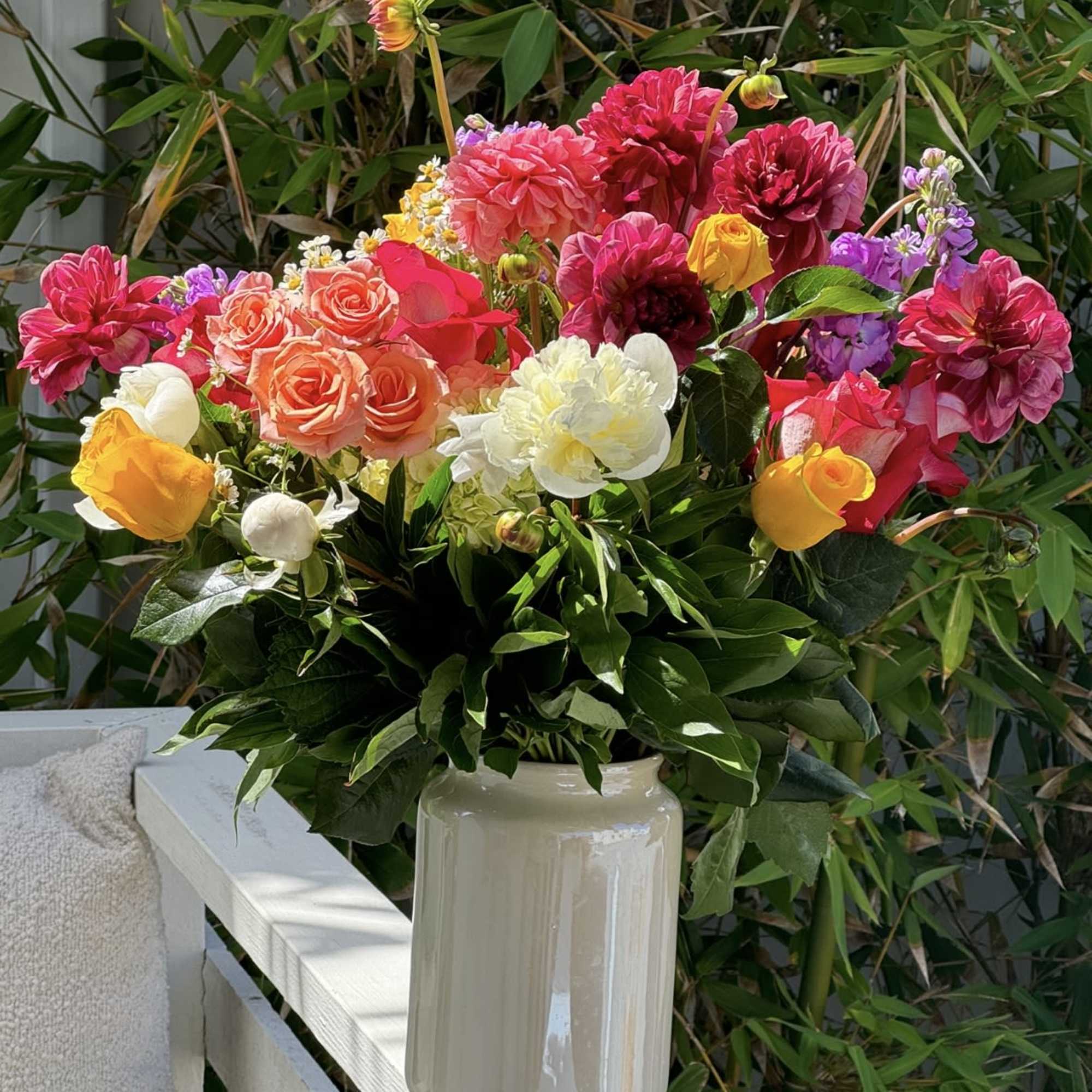 Bright mixed bouquet in a cream vase with pink, yellow, white, and purple blooms