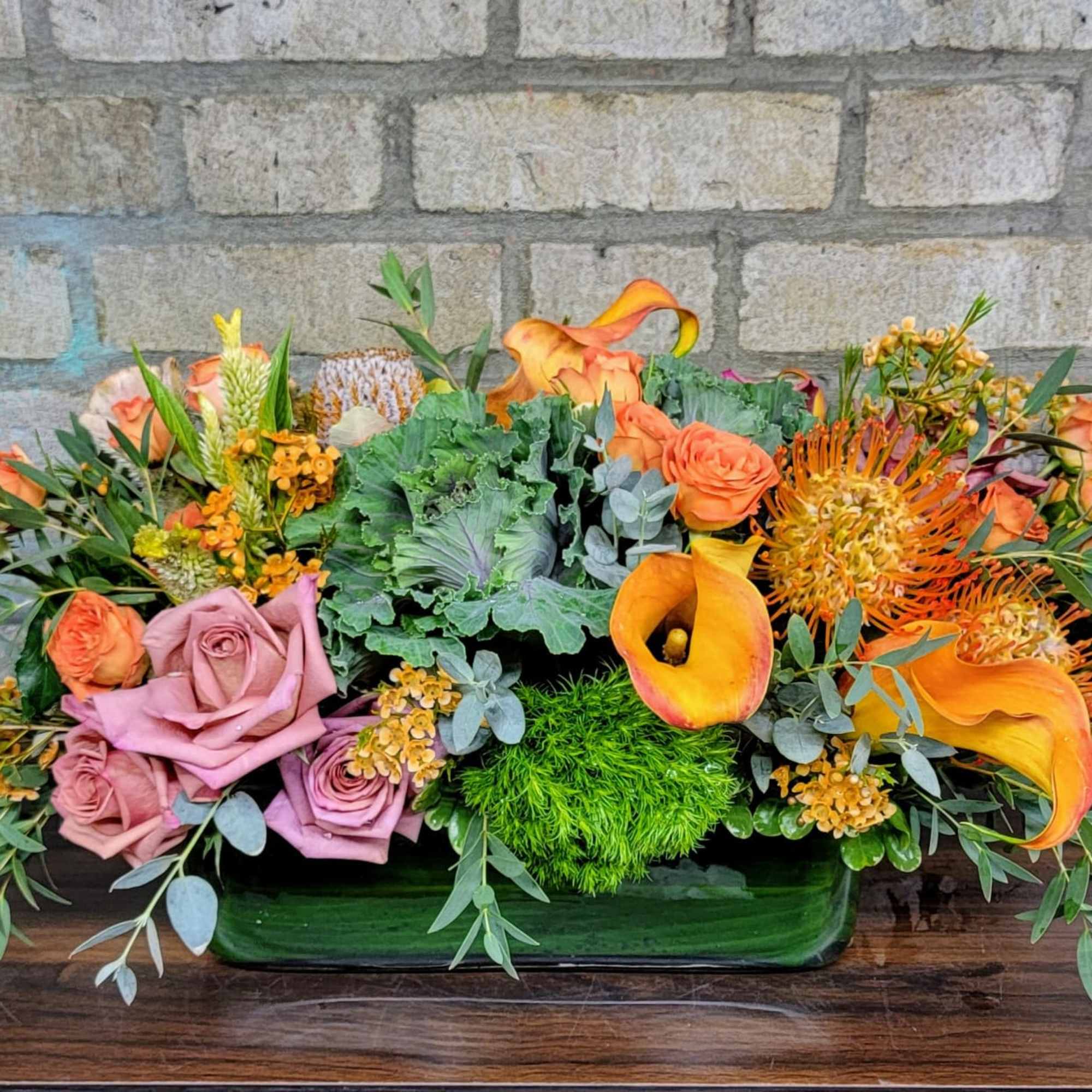 Orange and pink floral arrangement in a low green vase