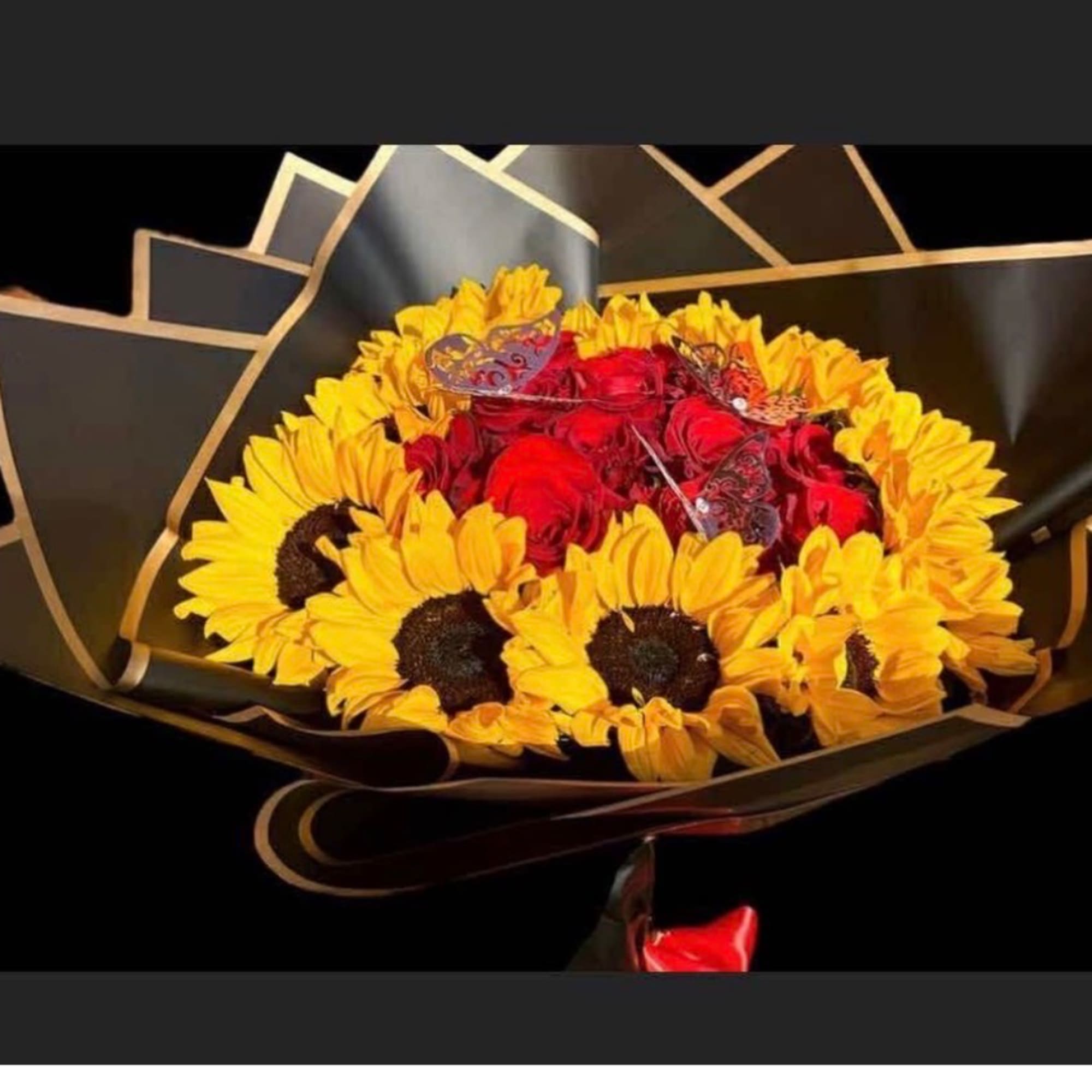 Bouquet of red roses surrounded by yellow sunflowers in black wrap
