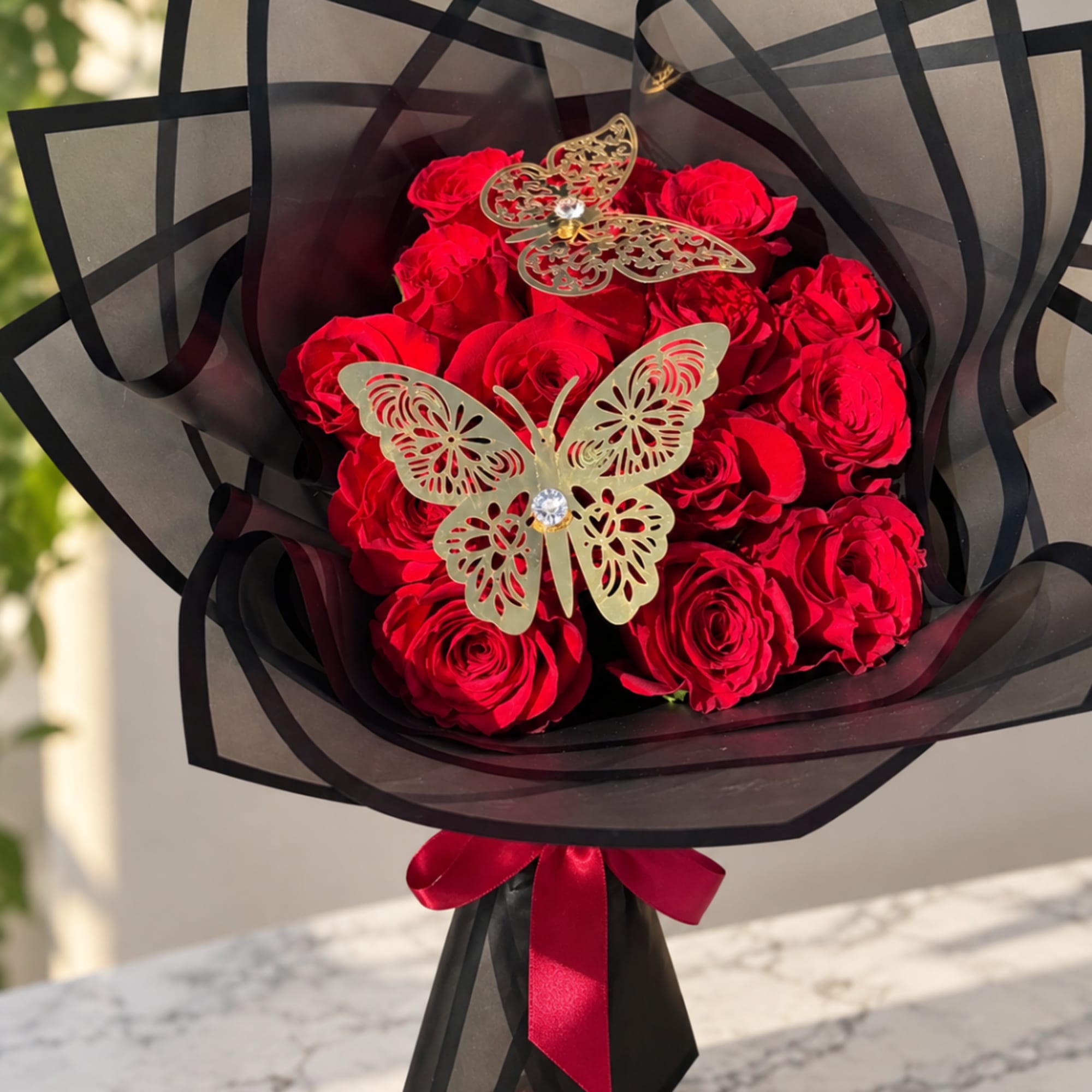 Bouquet of red roses wrapped in black paper with butterfly decorations