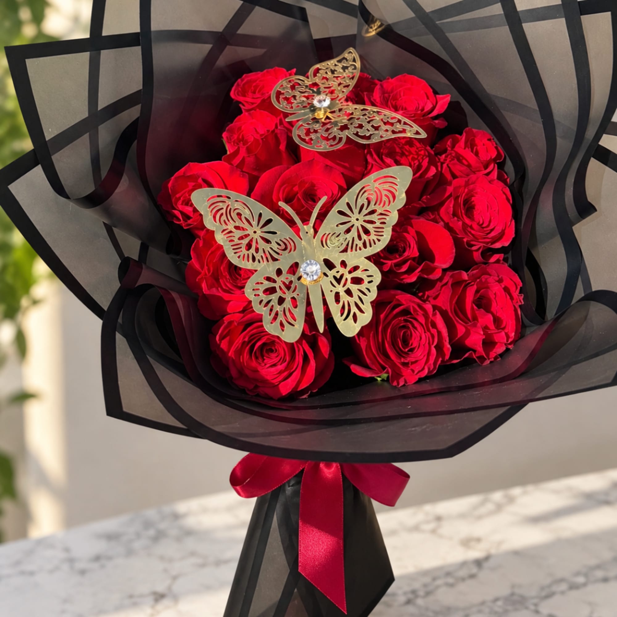 Bouquet of red roses wrapped in black paper with butterfly decorations