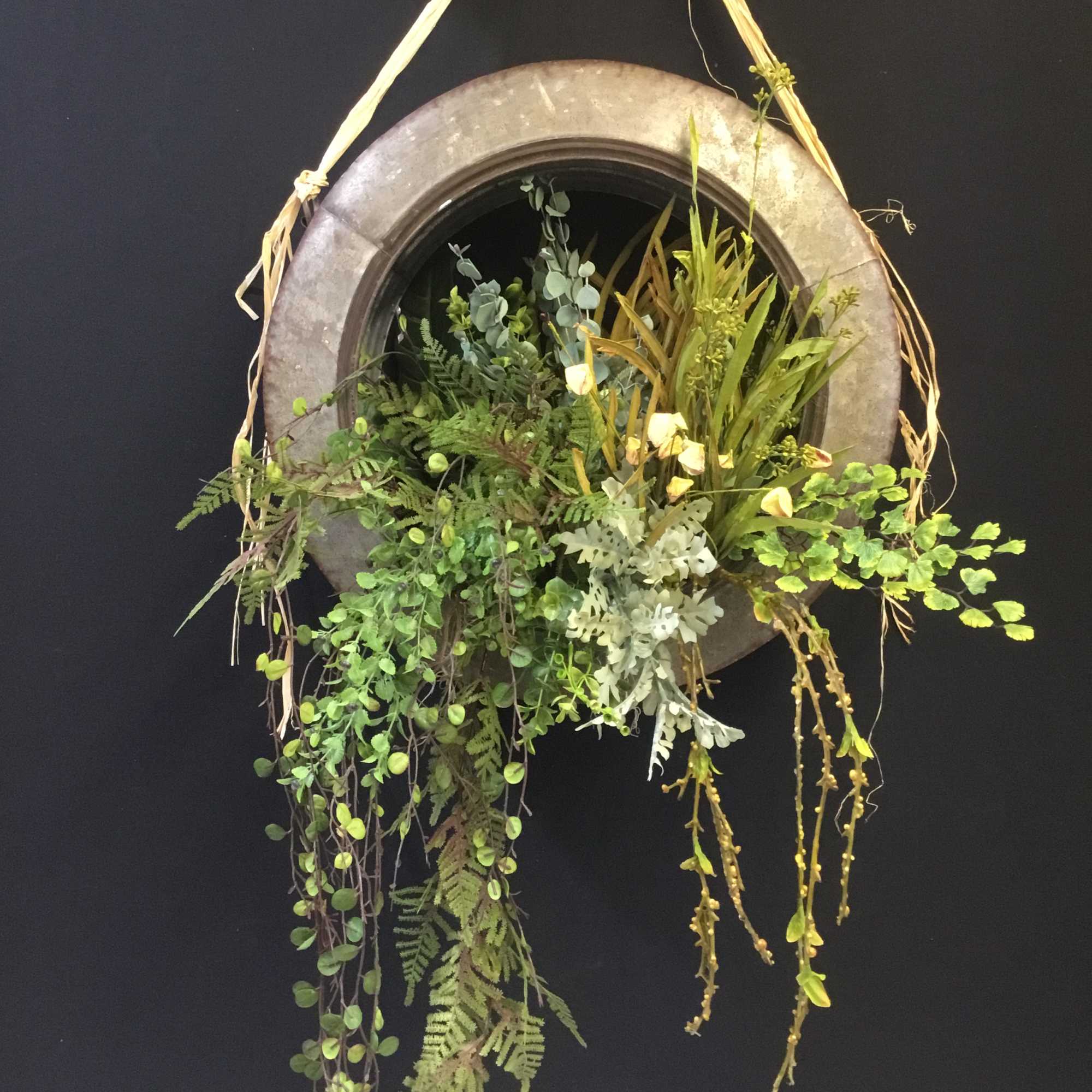 Hanging greenery arrangement in a round metal frame with trailing foliage