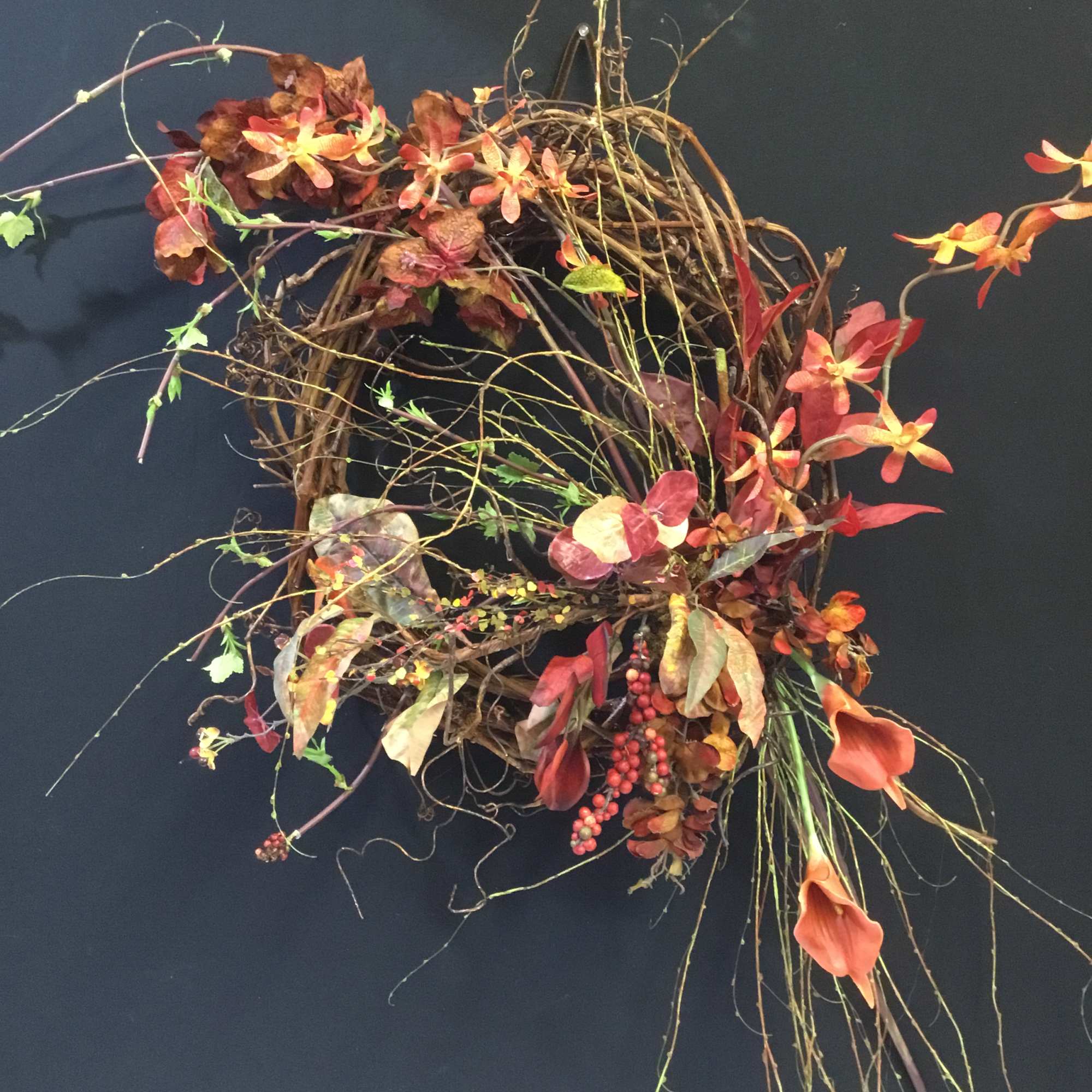 Autumn wreath with orange flowers and twisting branches on a dark wall