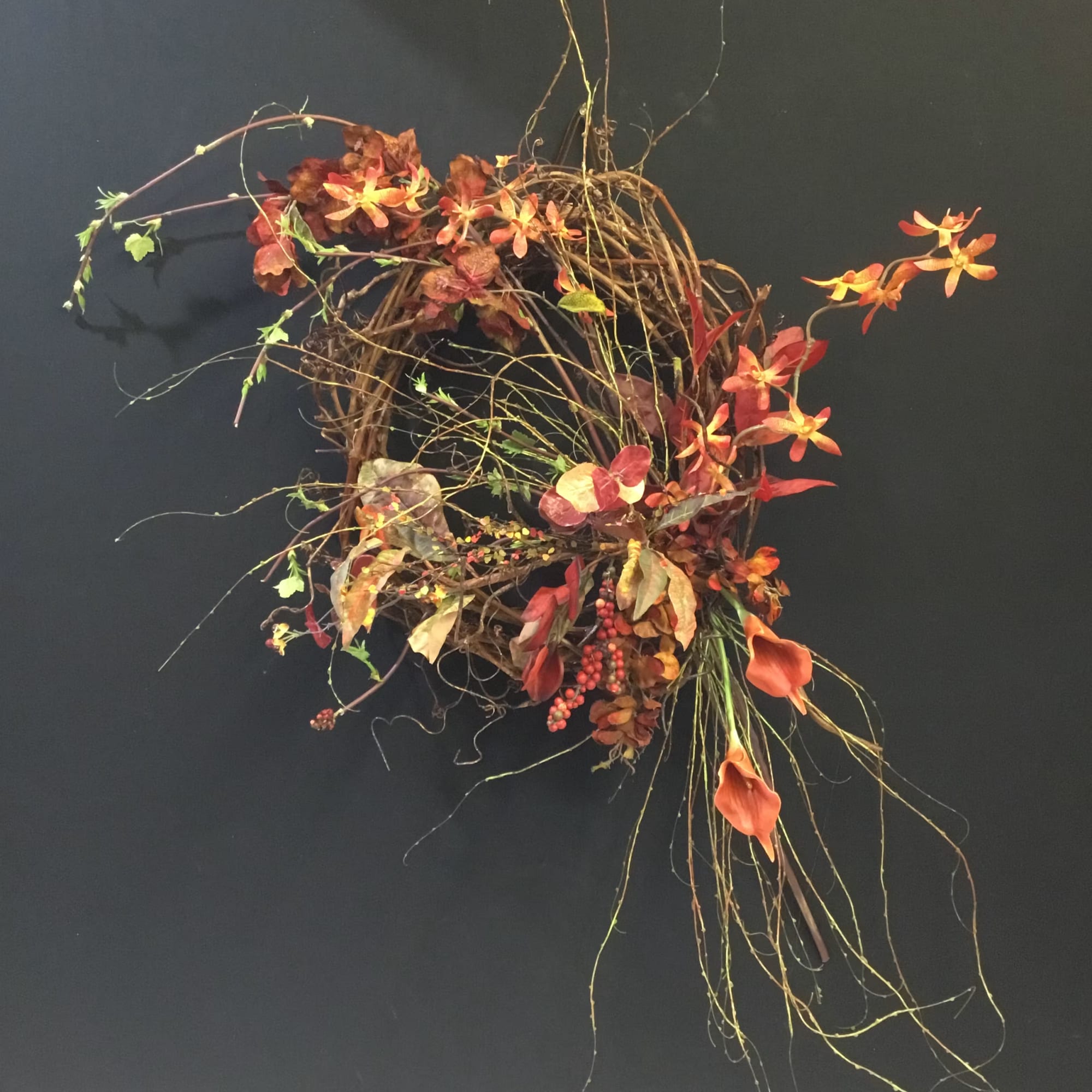Abstract floral wreath with orange blooms and trailing vines on a dark background