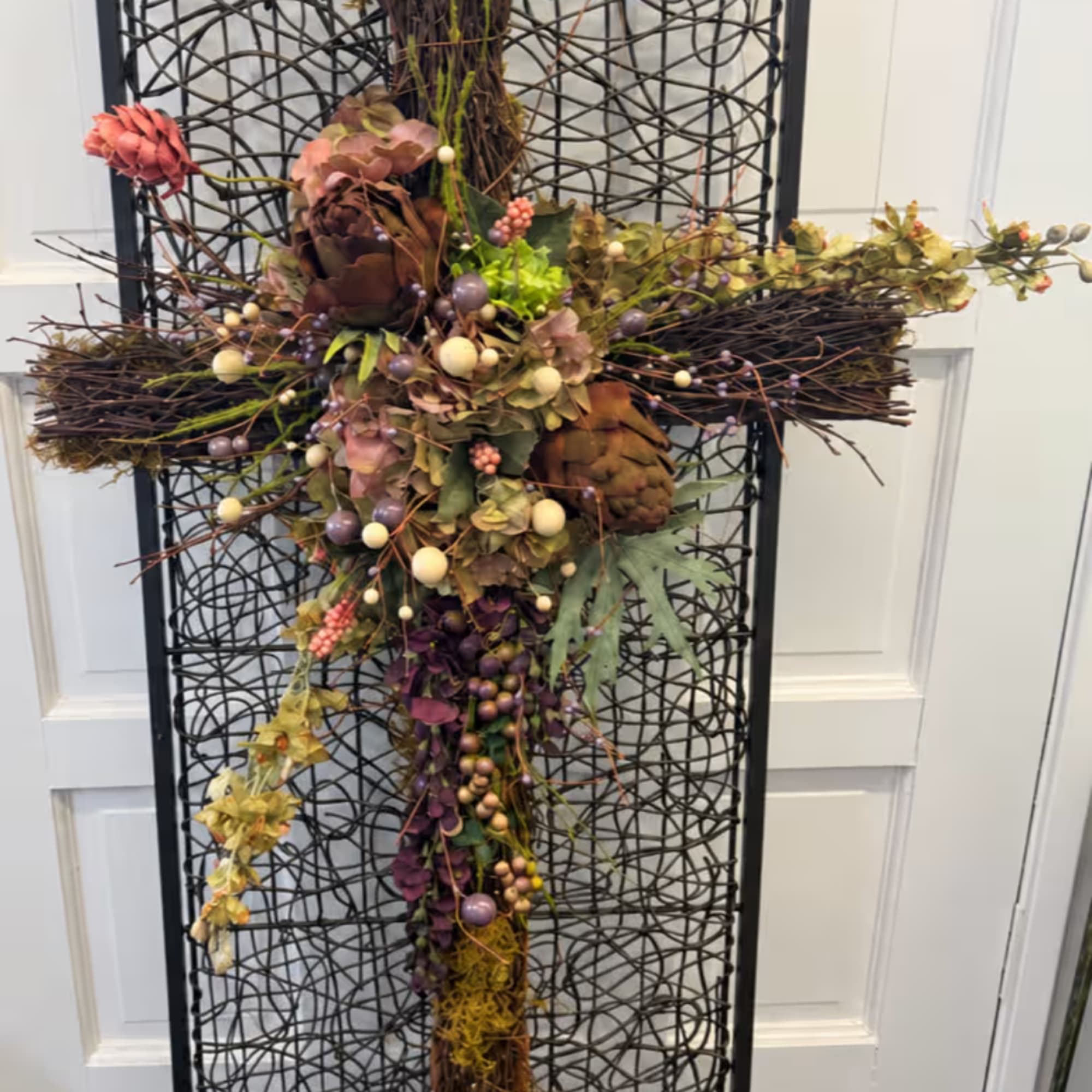 Decorative cross made of dried flowers and berries on a black lattice frame