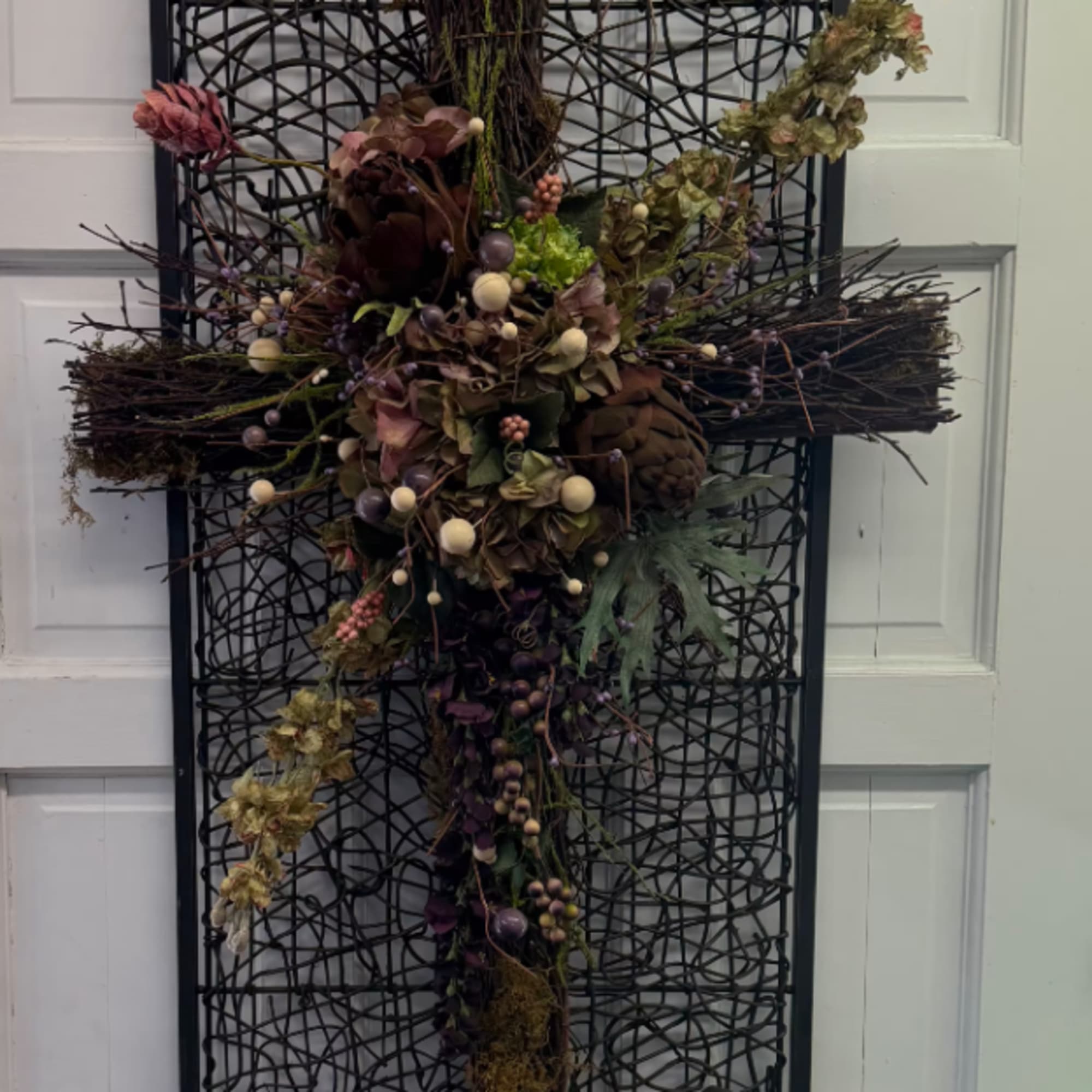 Dried floral cross arrangement mounted on a black lattice panel