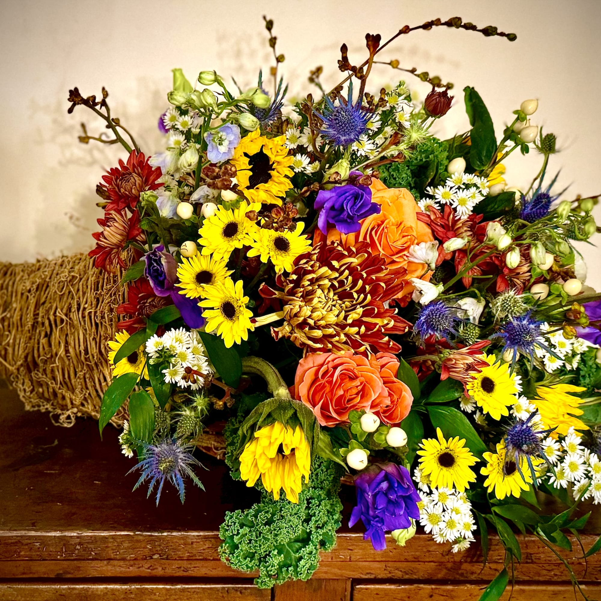 Colorful fall cornucopia arrangement with yellow sunflowers, orange roses, and mixed blooms in a woven horn basket