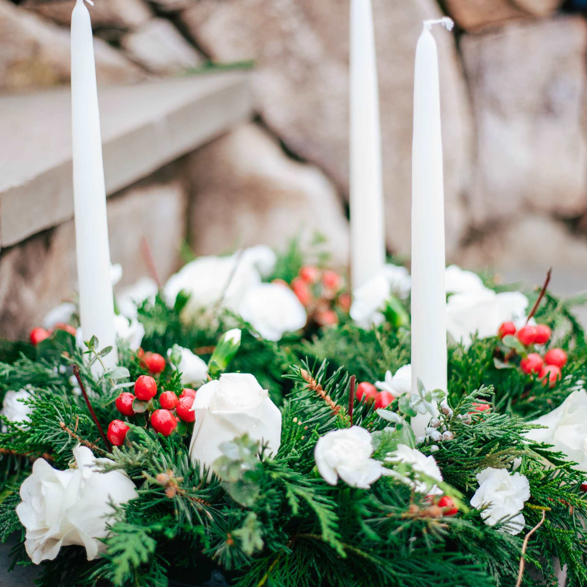 Evergreen candle ring with white flowers, red berries, and three white taper candles