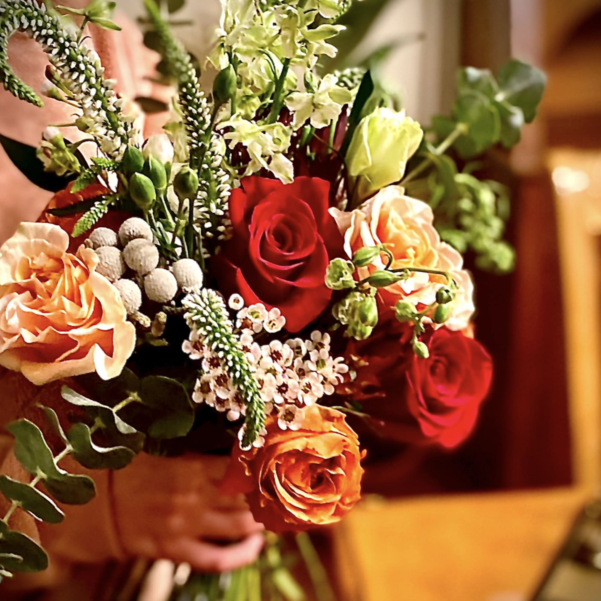 Hand-tied bouquet with red and orange roses, peach blooms, and small white accent flowers.