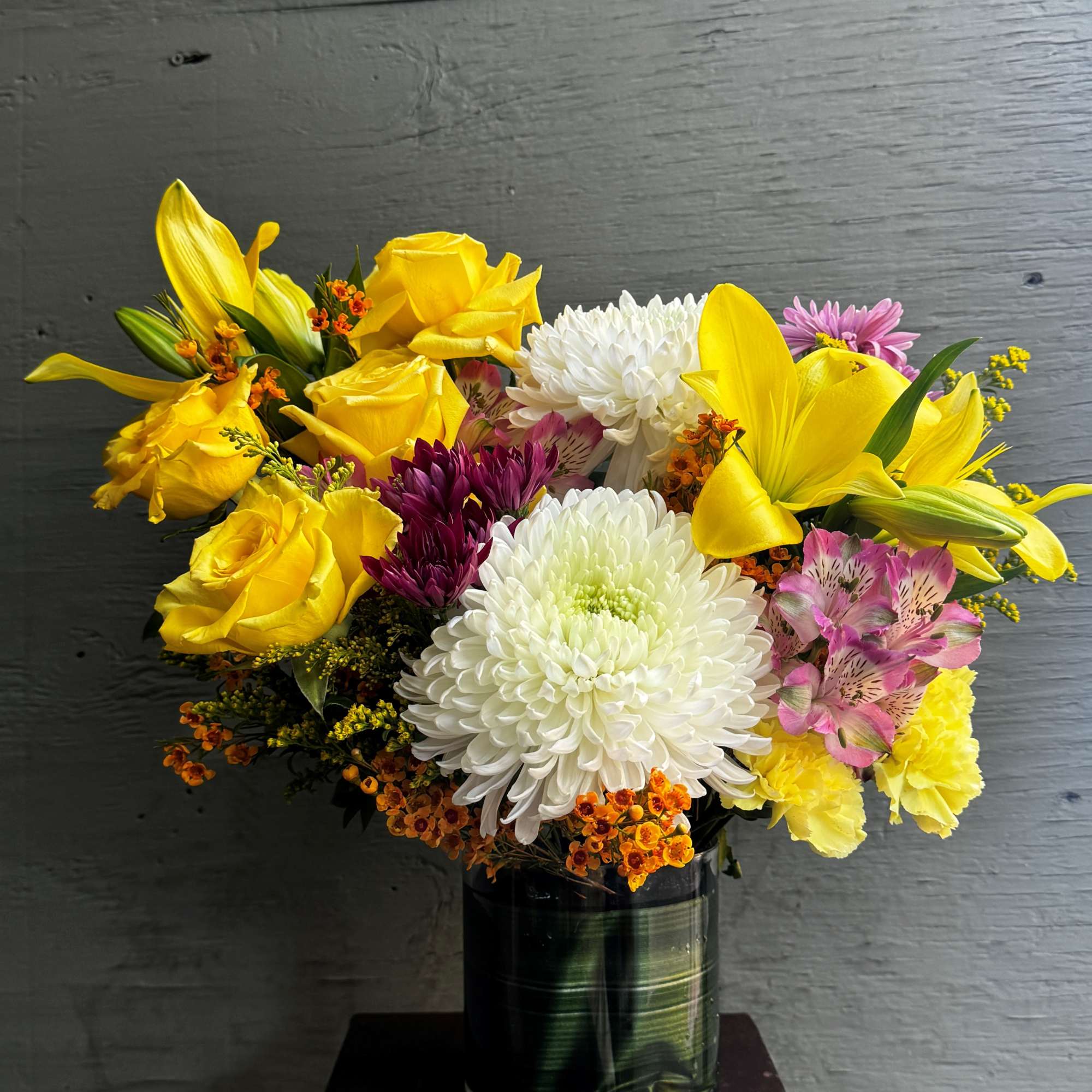 Bouquet of yellow roses, white chrysanthemums, and lilies in a glass vase