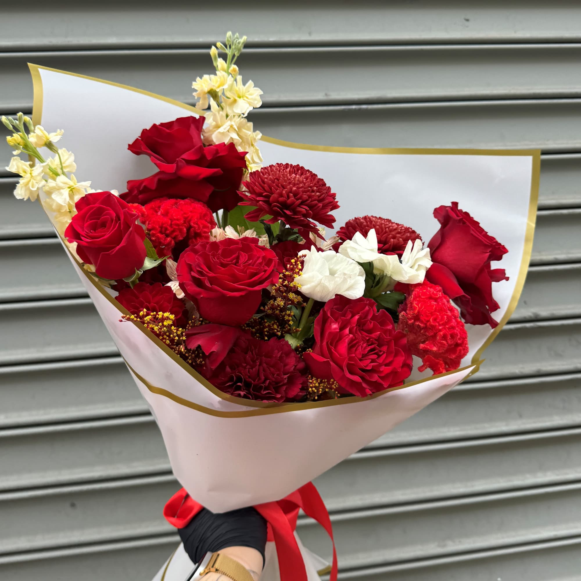 Bouquet of red roses, red carnations, and white flowers wrapped in white paper