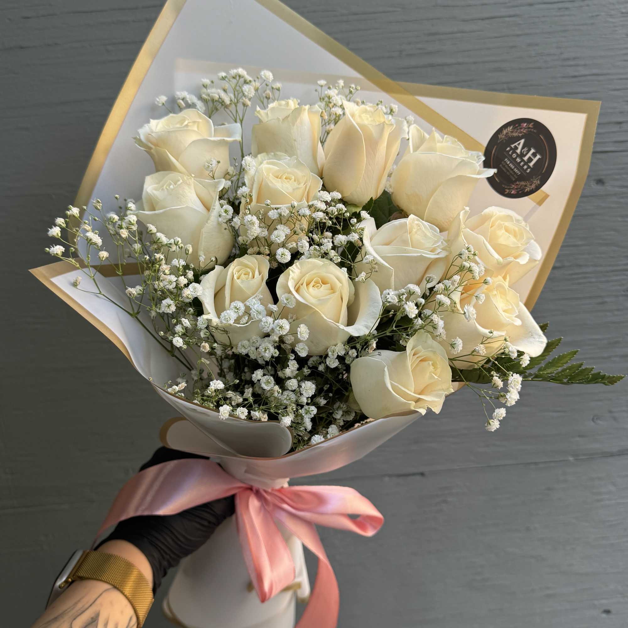 Bouquet of cream roses with baby's breath wrapped in white paper and a pink ribbon