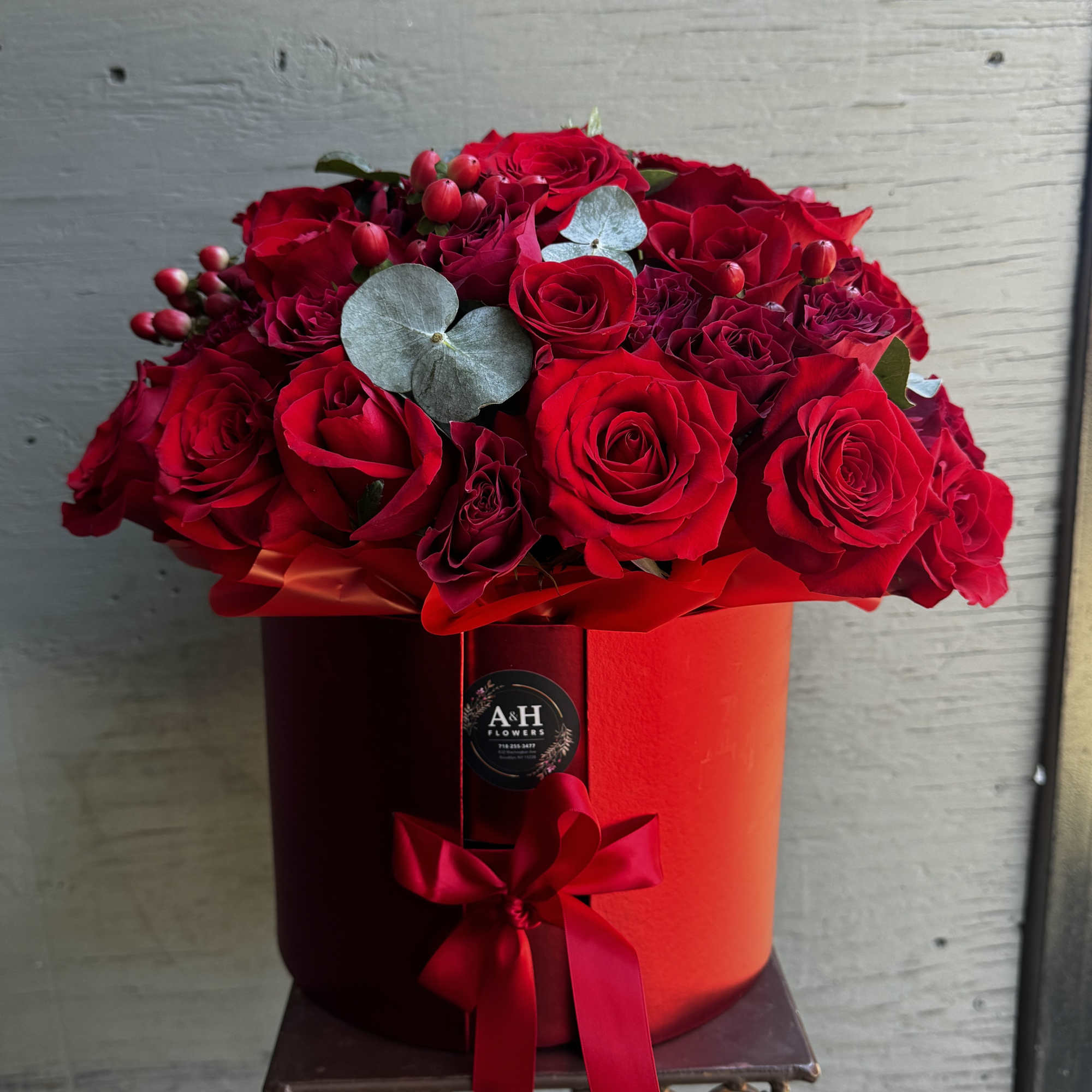 Red roses arranged in a round red hat box with a ribbon