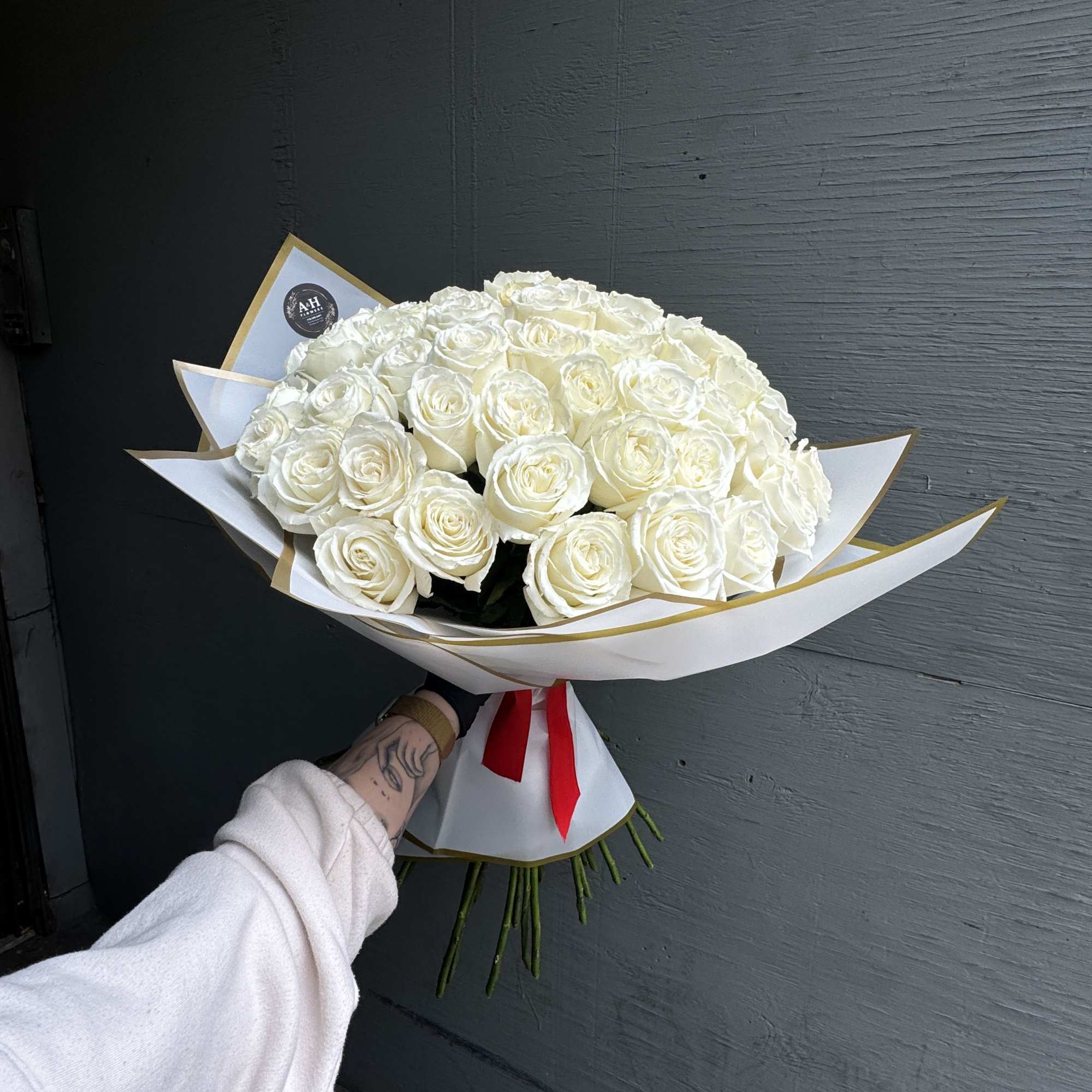 Large bouquet of white roses wrapped in white paper with a red ribbon