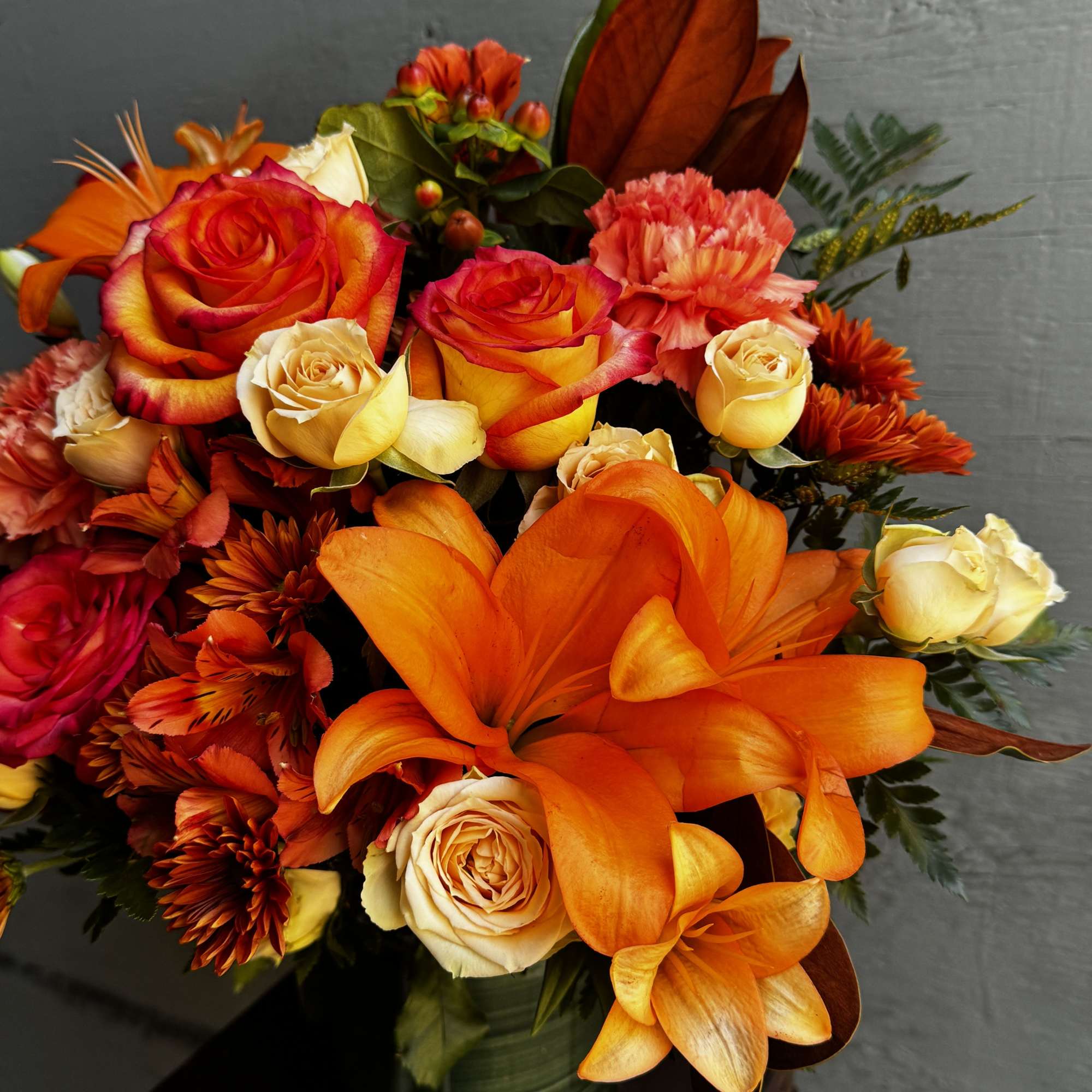 Orange lilies and roses arranged in a green vase