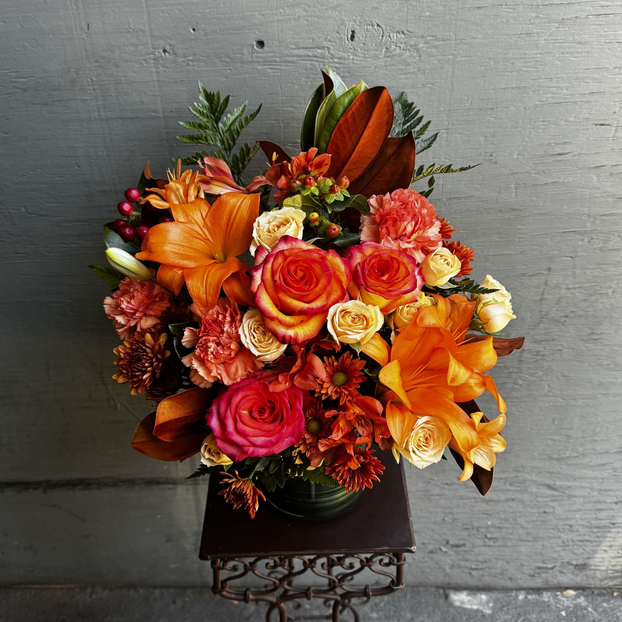 Bright orange and pink flower arrangement in a dark vase