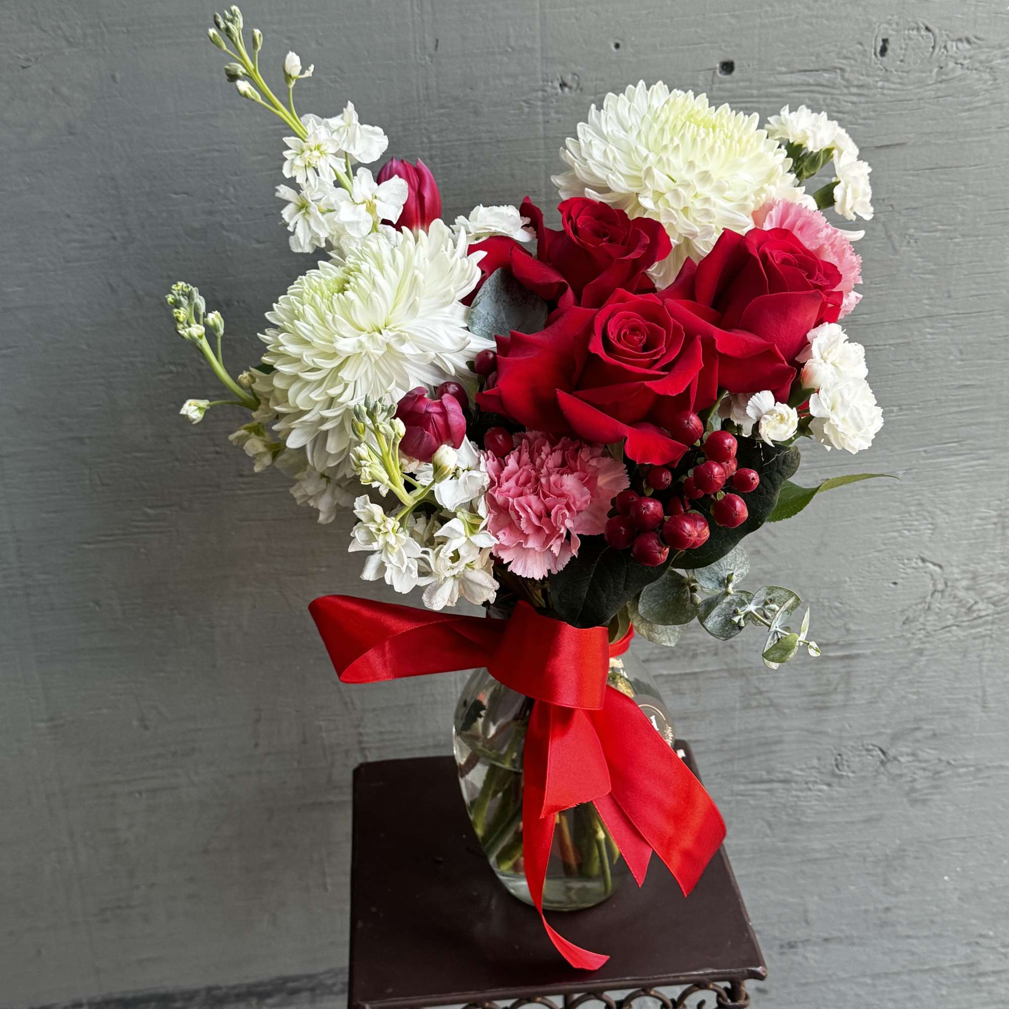 Bouquet of red roses and white chrysanthemums in a glass vase with a red ribbon